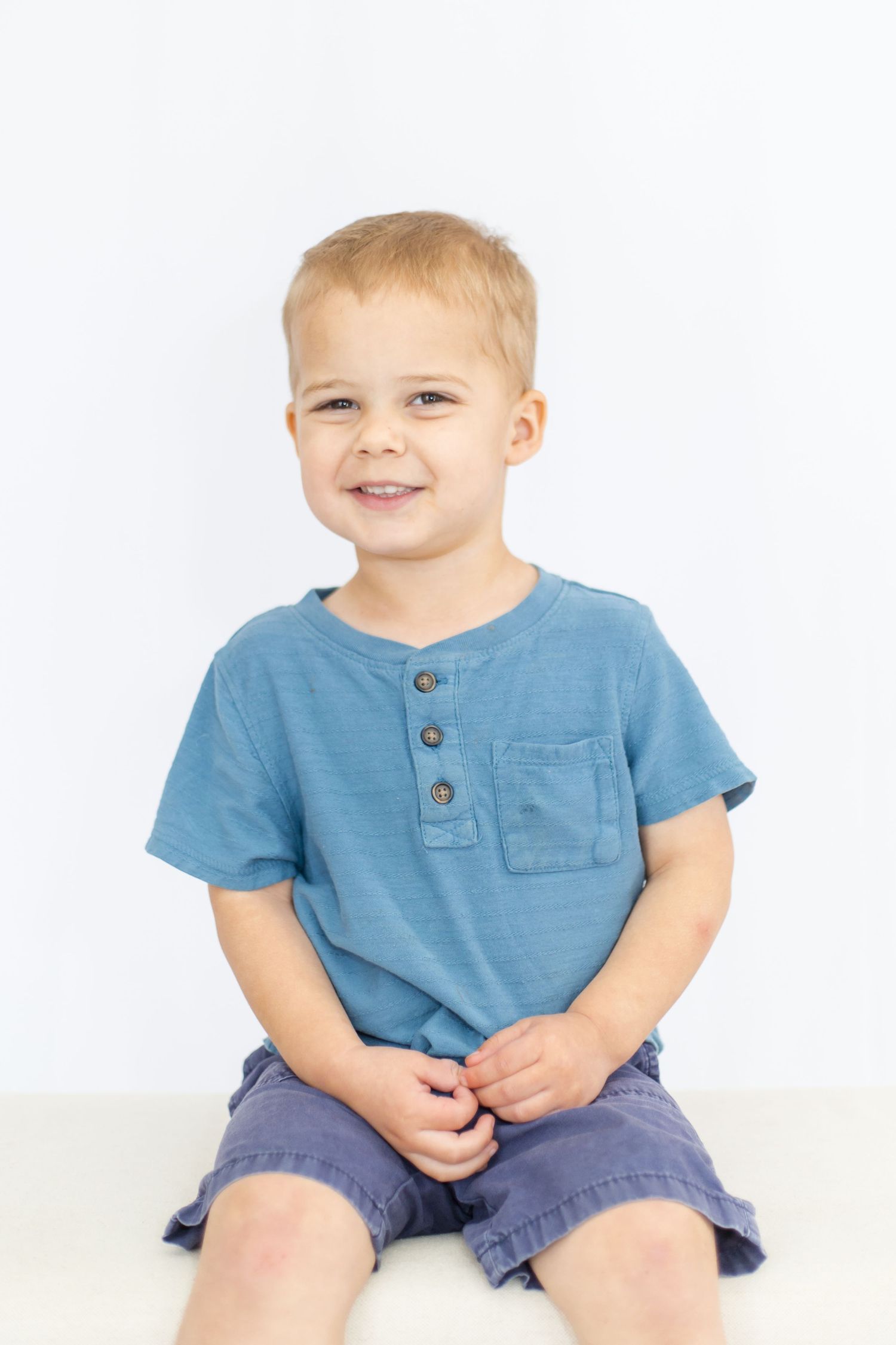 Child wearing blue shirt and navy shorts poses on white background.