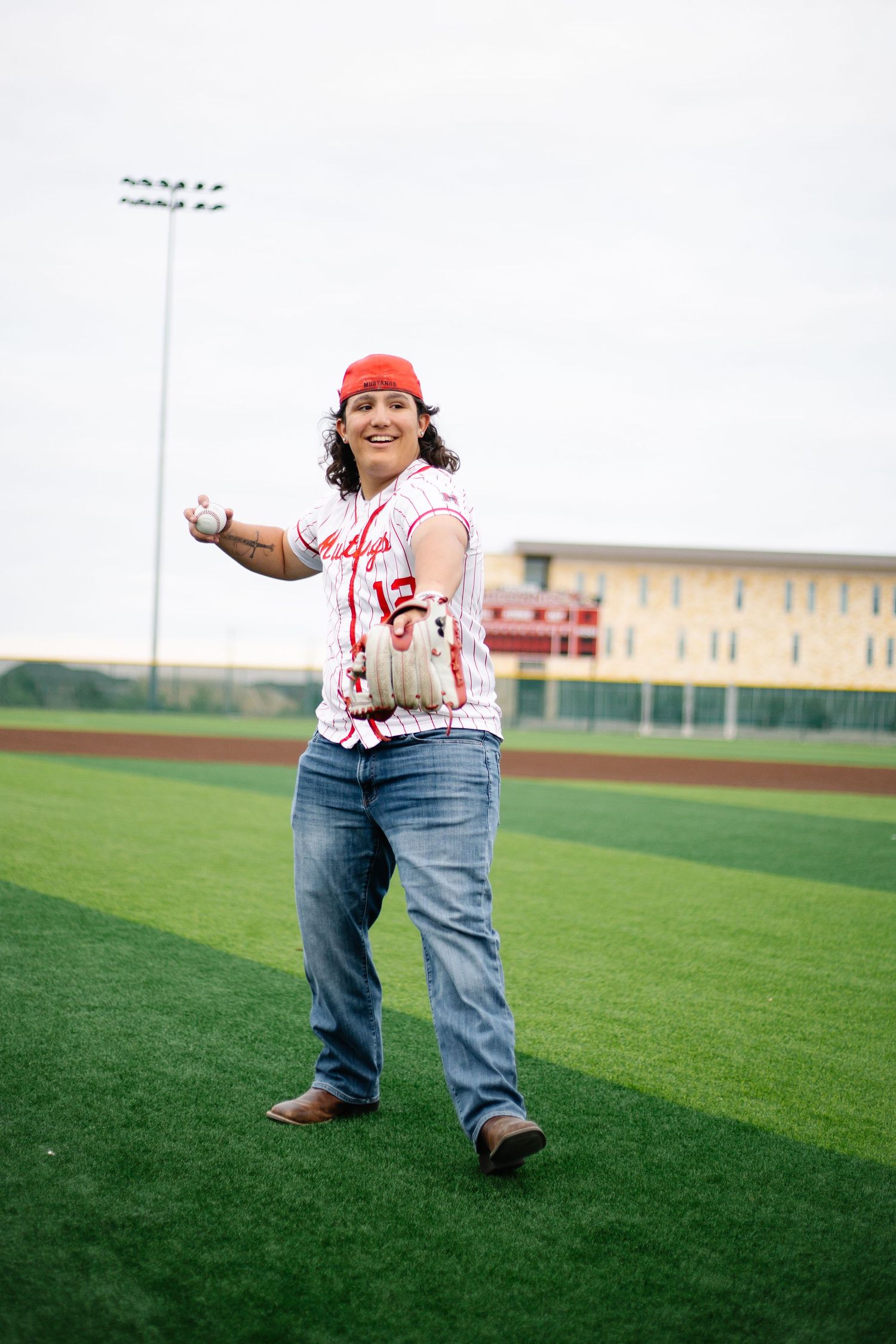 A smiling baseball player in a red cap and jersey prepares to throw a ball on a green turf field.