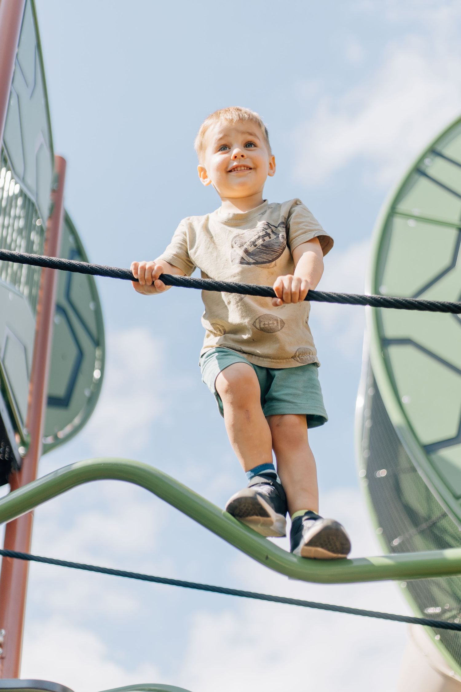Child climbing on outdoor playground equipment against blue sky.