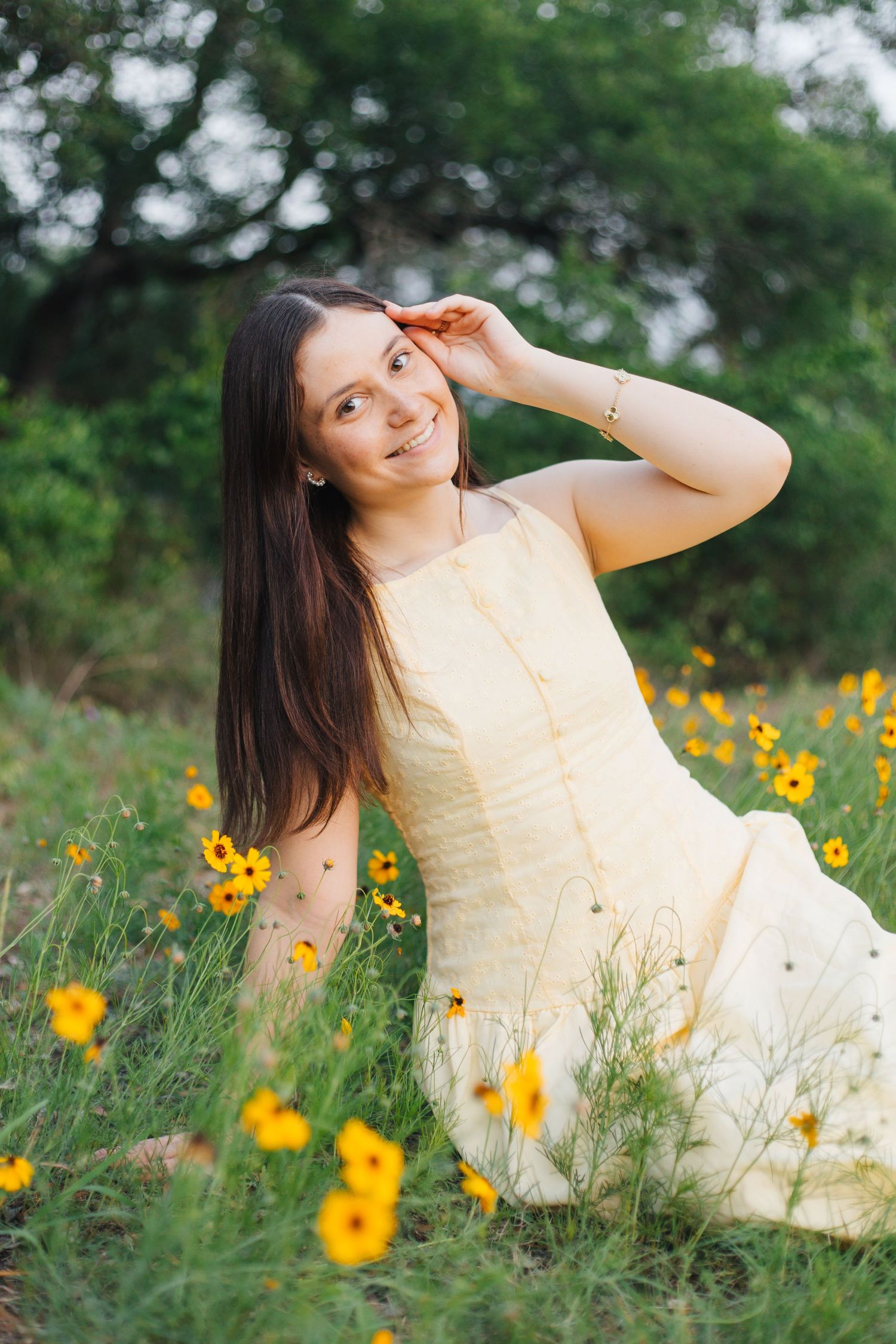 Young woman in yellow sundress sitting in a field of yellow wildflowers, smiling in golden afternoon light Senior Portraits Round Rock TX
