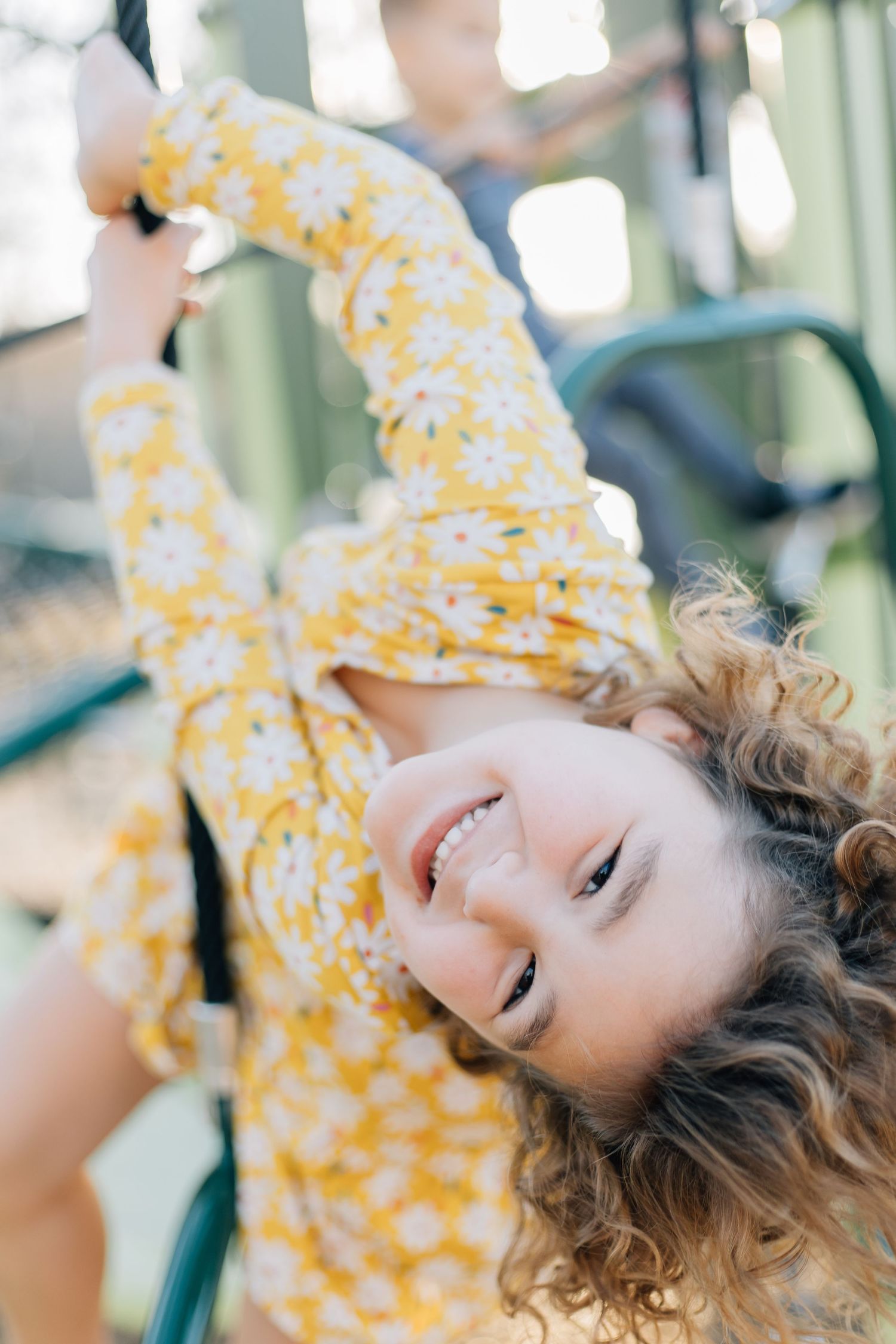Person in yellow floral dress playing joyfully on playground equipment.