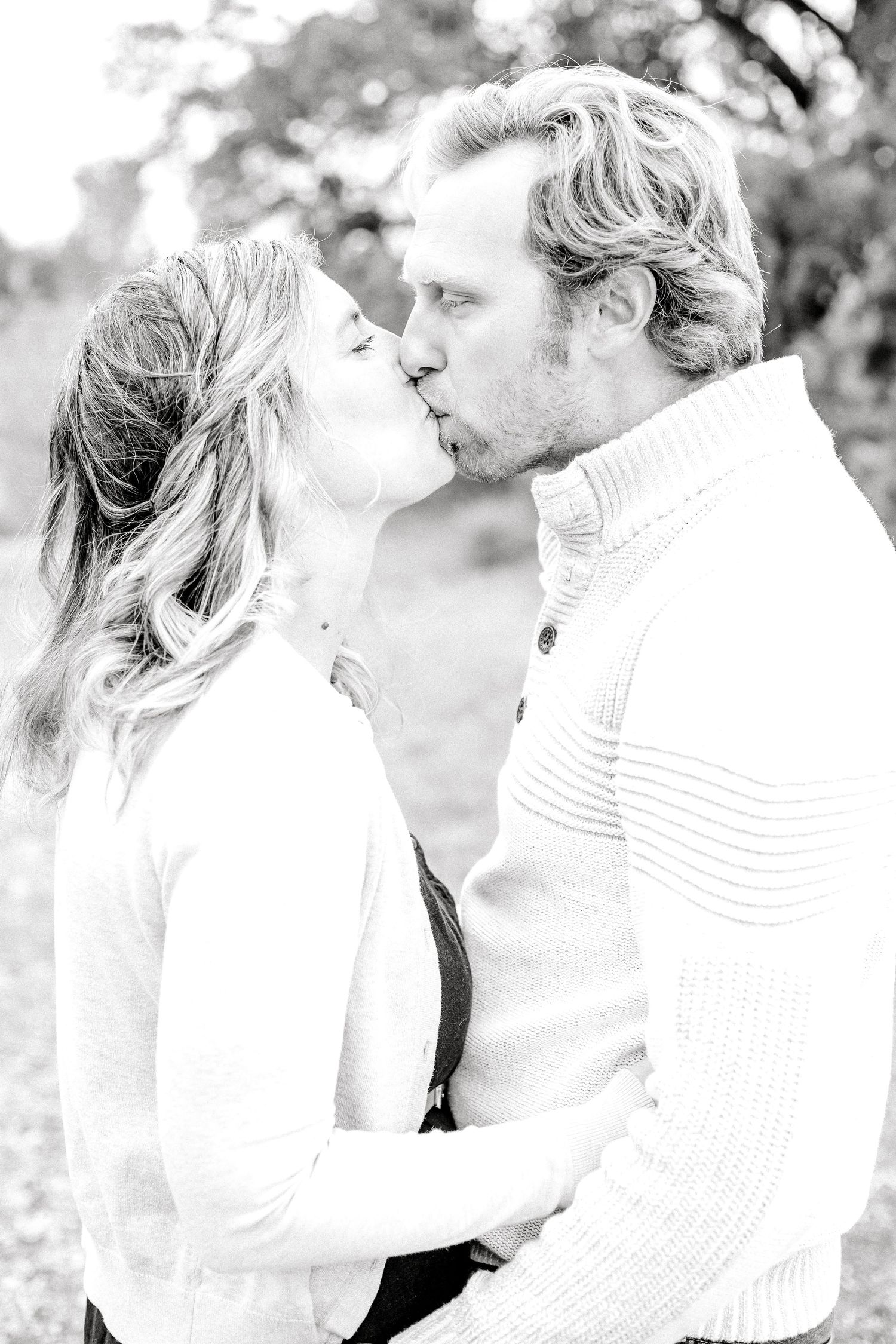 A romantic black and white portrait of a couple sharing an intimate kiss outdoors.