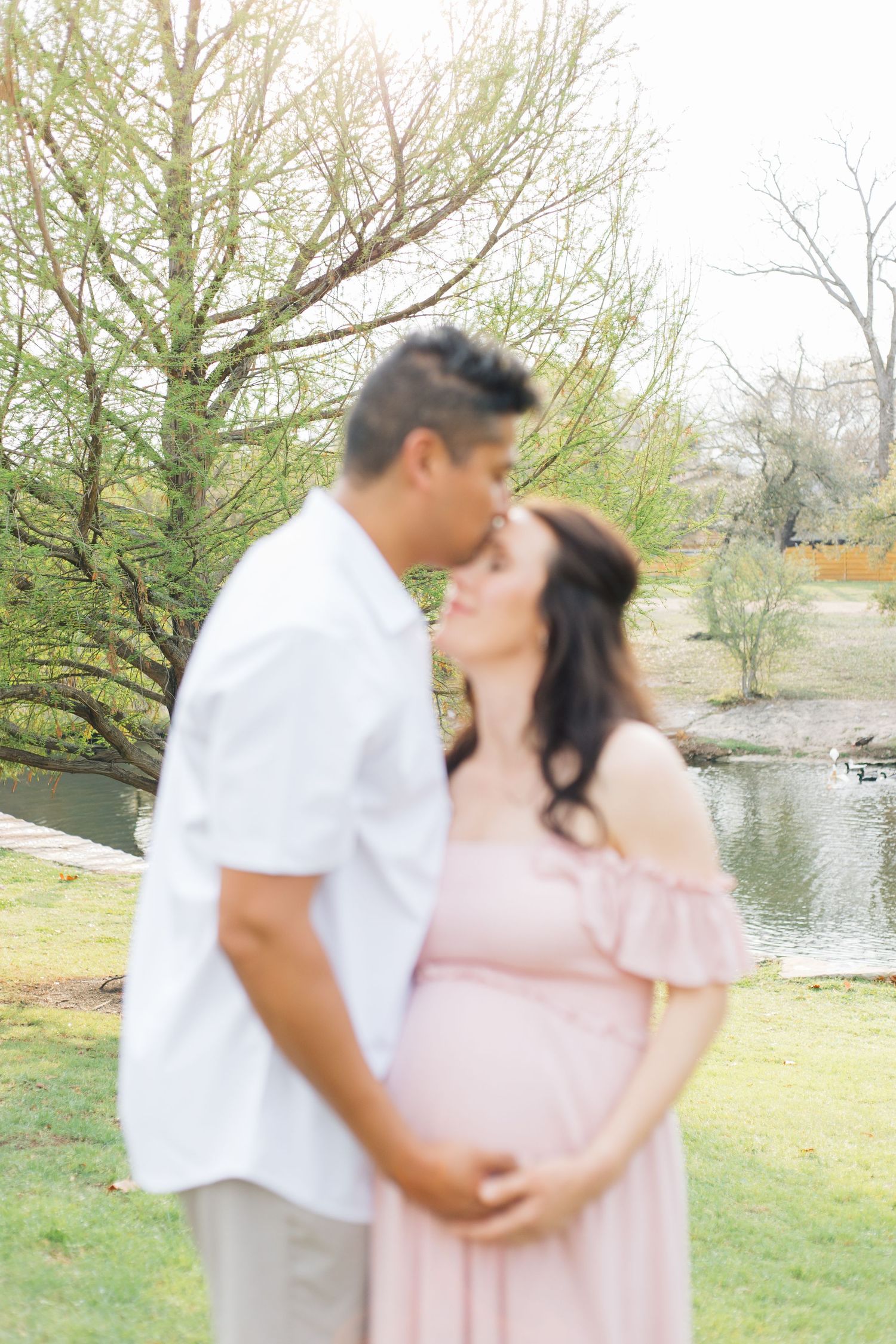 A couple embraces in a romantic outdoor photoshoot near a lake with trees in the background.