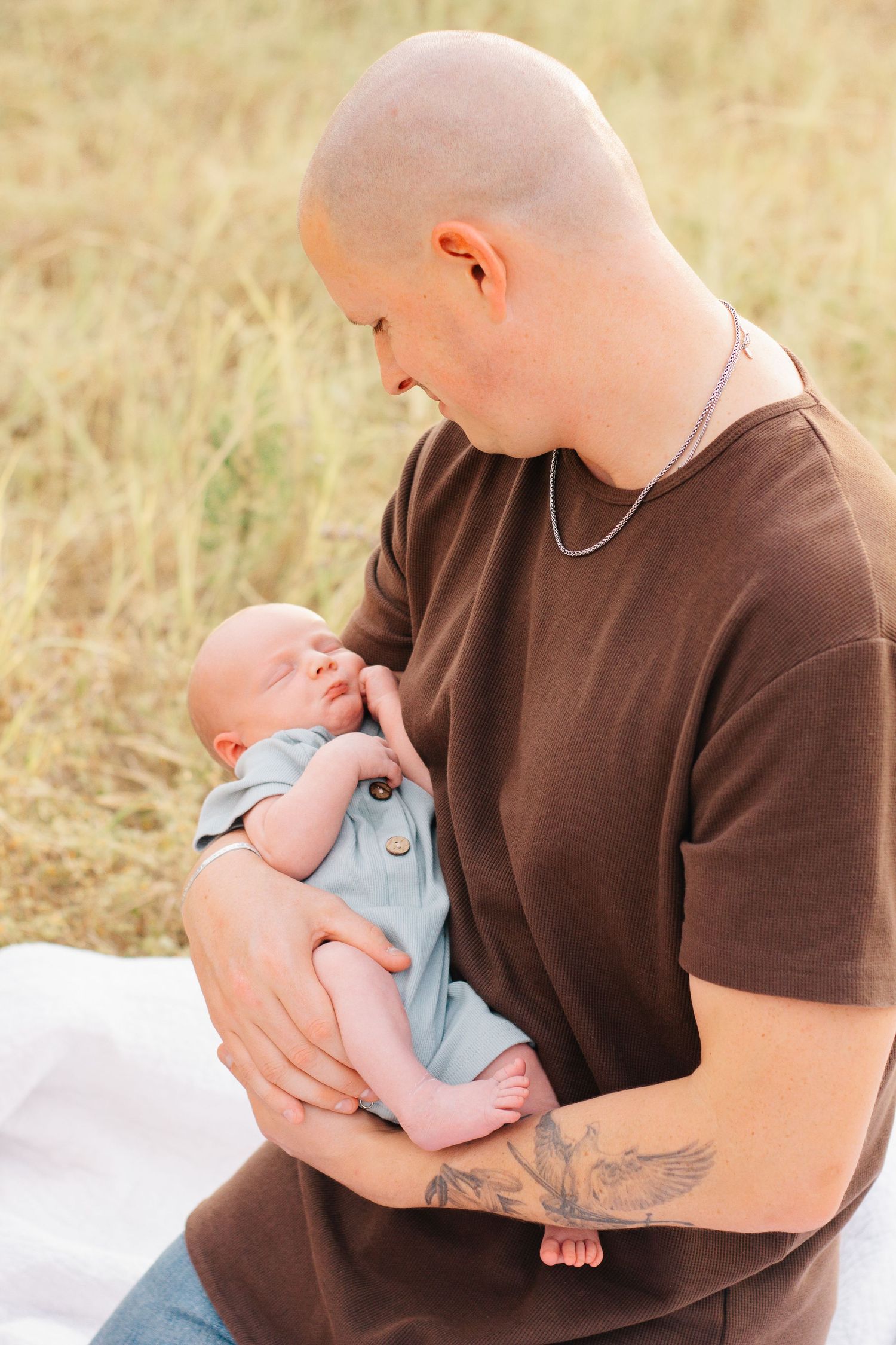 Parent in brown shirt holding and bonding with baby on white blanket outdoors.