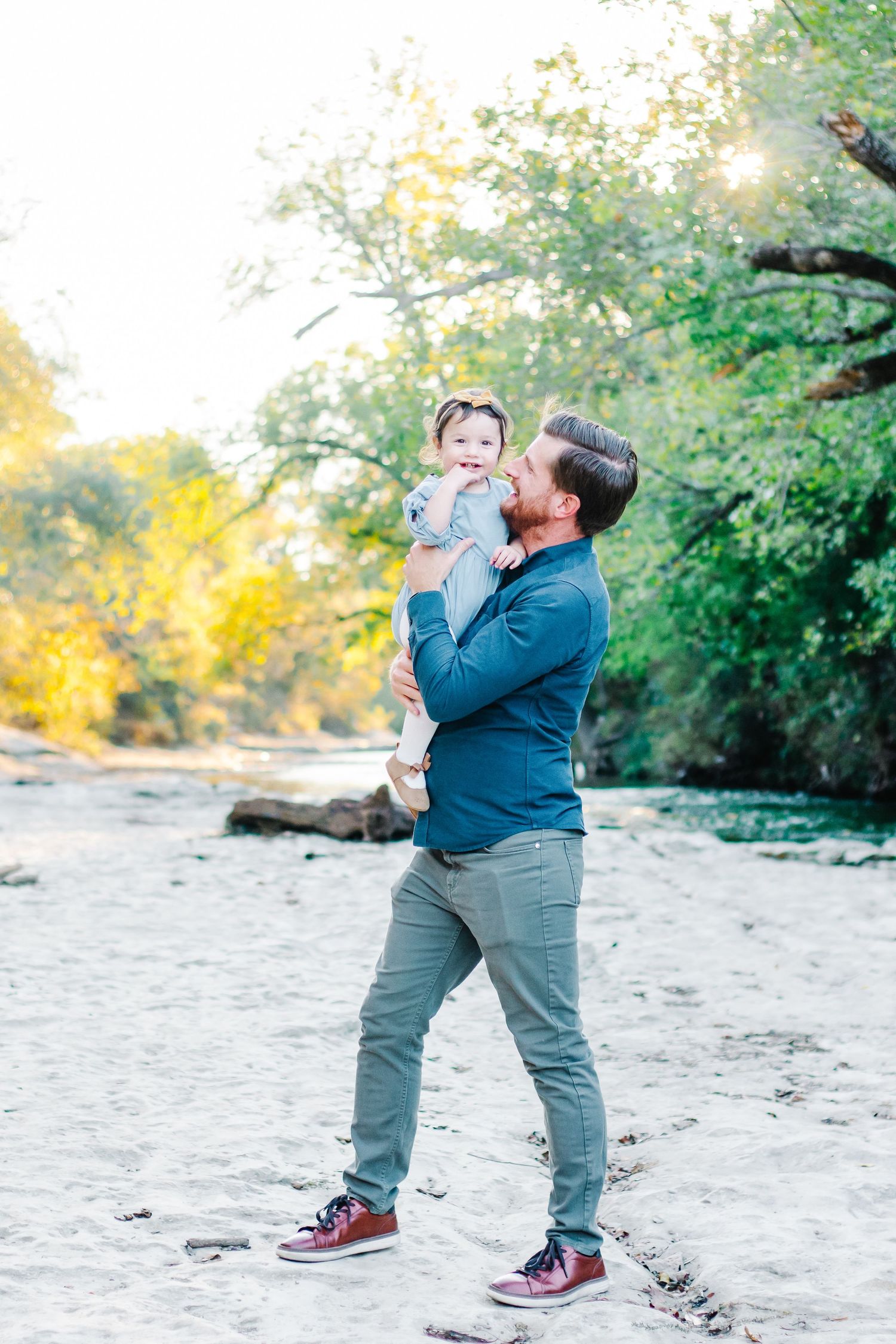 Parent and child playing together on sandy beach during sunset with trees in background.