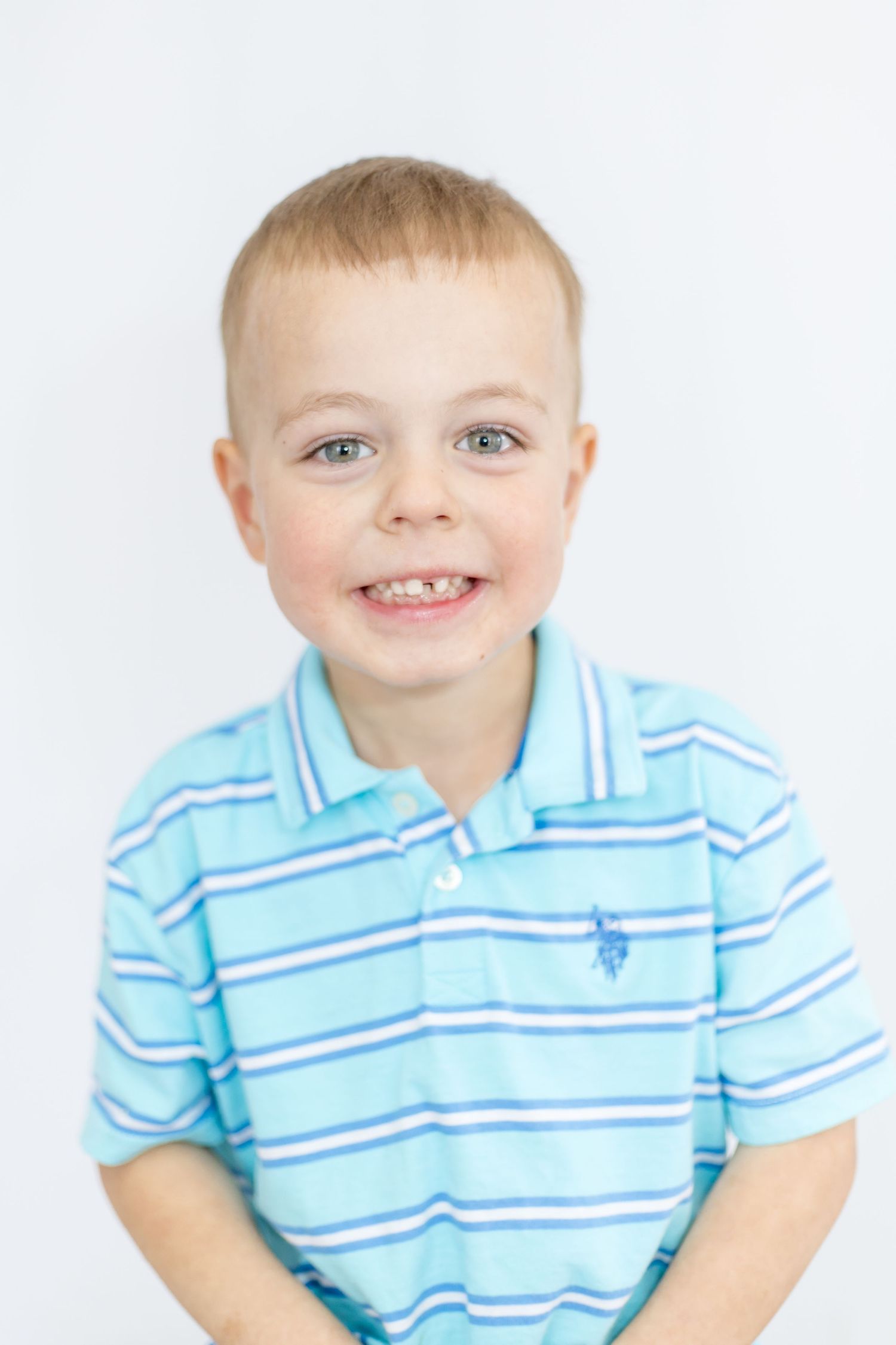 Child wearing light blue and white striped polo shirt smiling at camera.