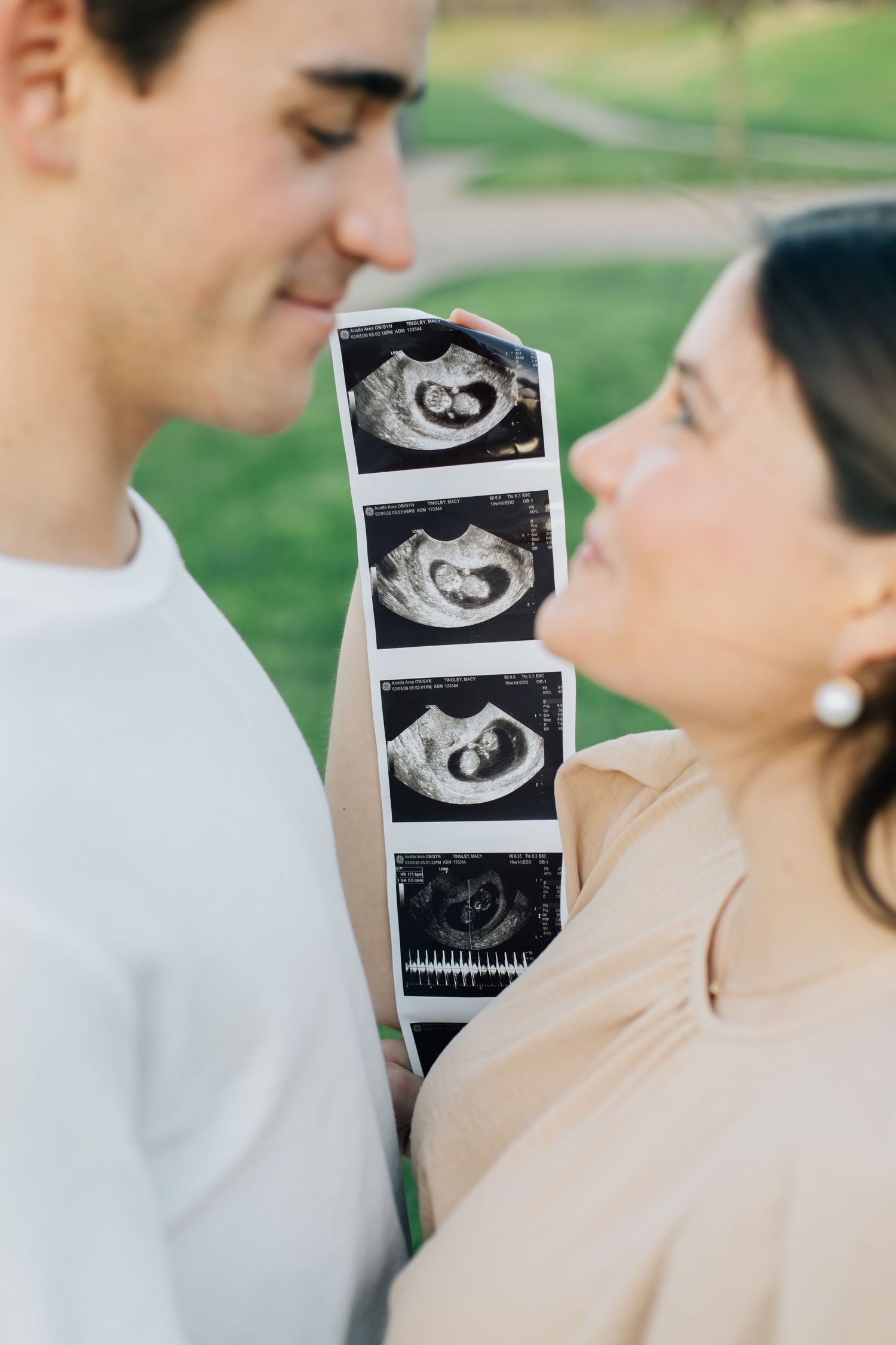 Close-up of couple looking at each other while holding strip of ultrasound images.