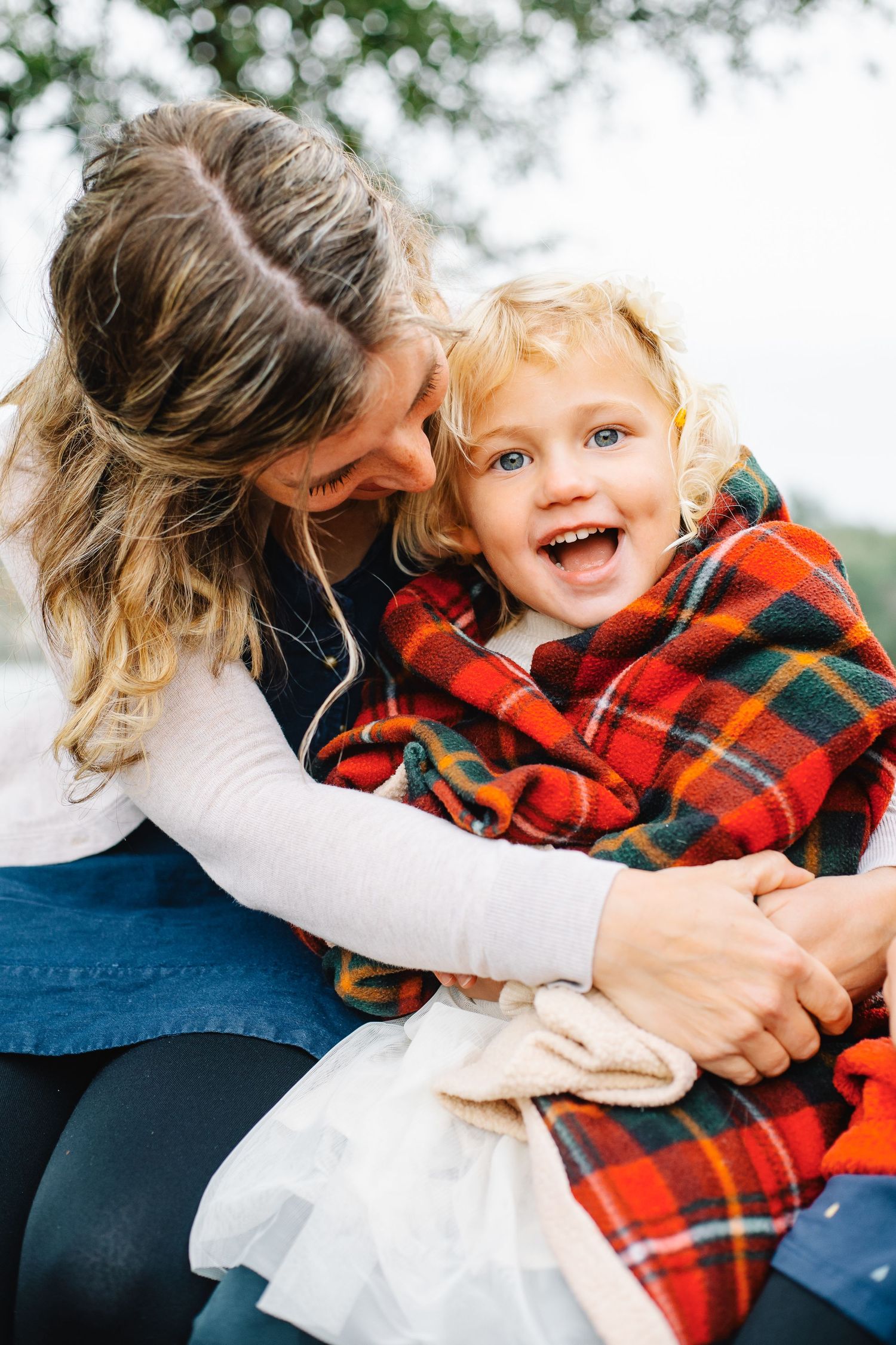 A joyful moment captured between parent and child wrapped in a plaid blanket outdoors.