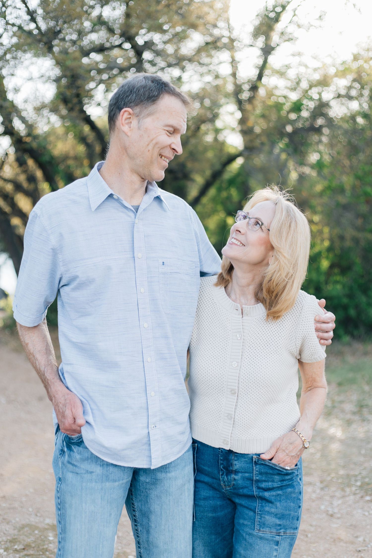 Smiling middle-aged couple walking together on a dirt path surrounded by trees.