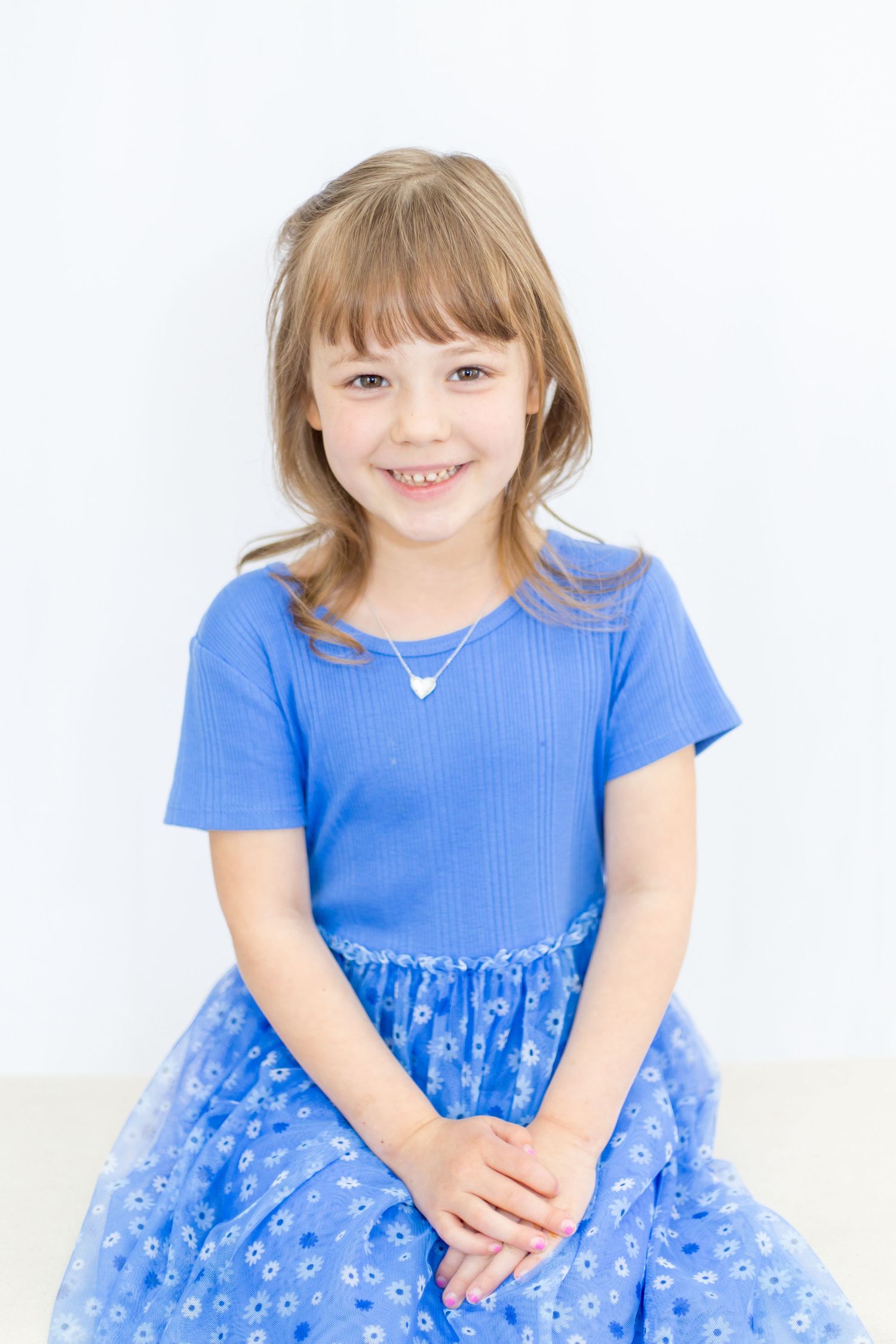 Young child in bright blue dress poses against white background.