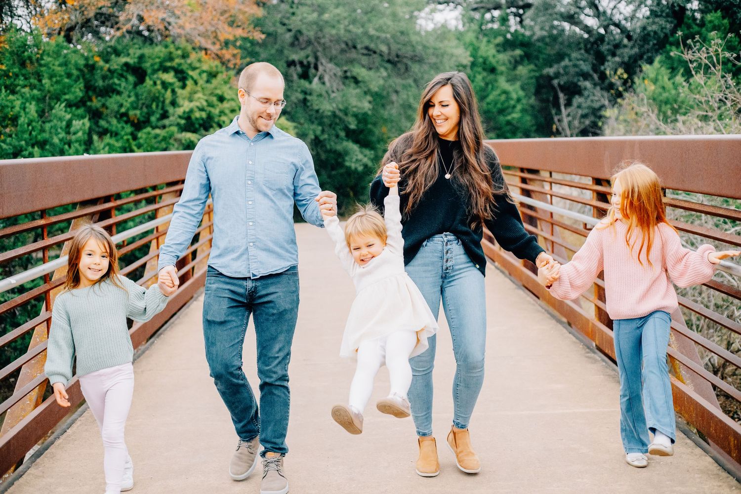 Family walking together on a wooden bridge in casual summer outfits.