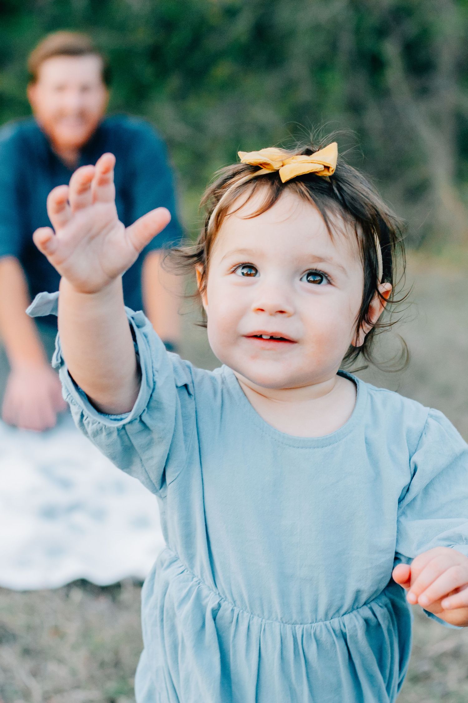 Sequence of a toddler in a light blue dress making expressive hand gestures against a natural background.