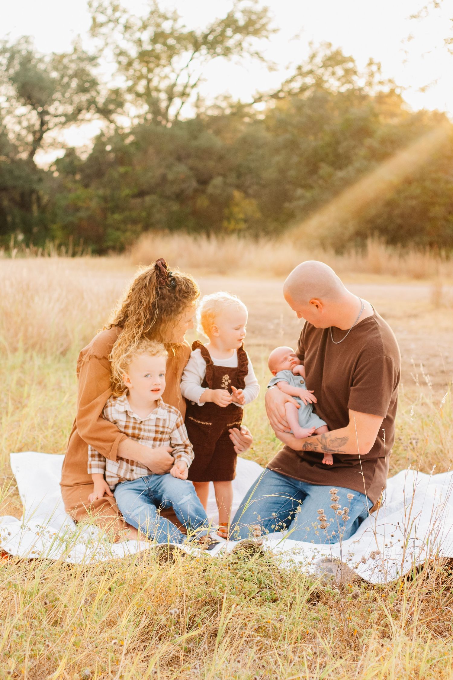 Family sitting together on blanket in golden field during sunset photo session.