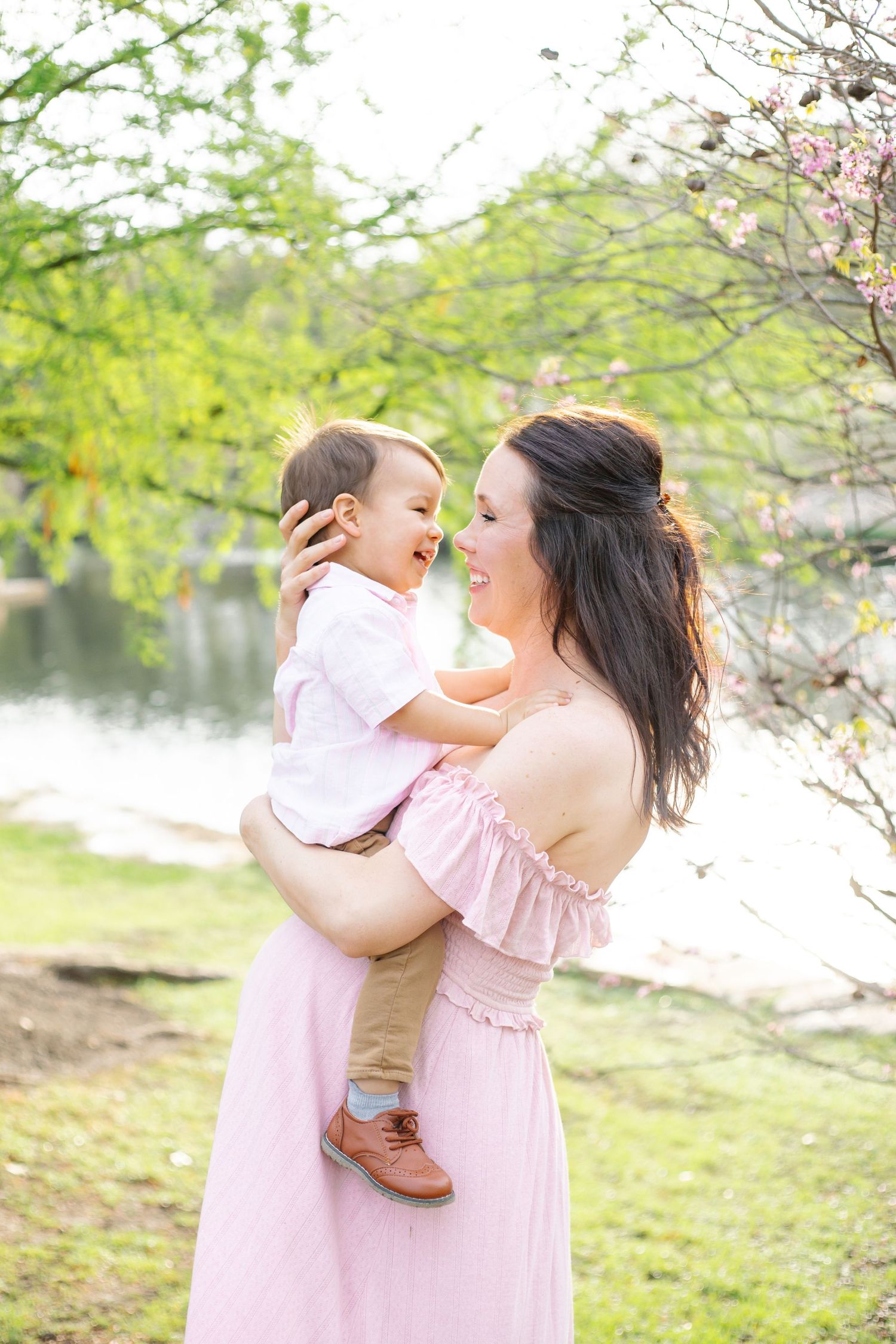 A mother and child share playful moments during a springtime photoshoot with cherry blossoms.