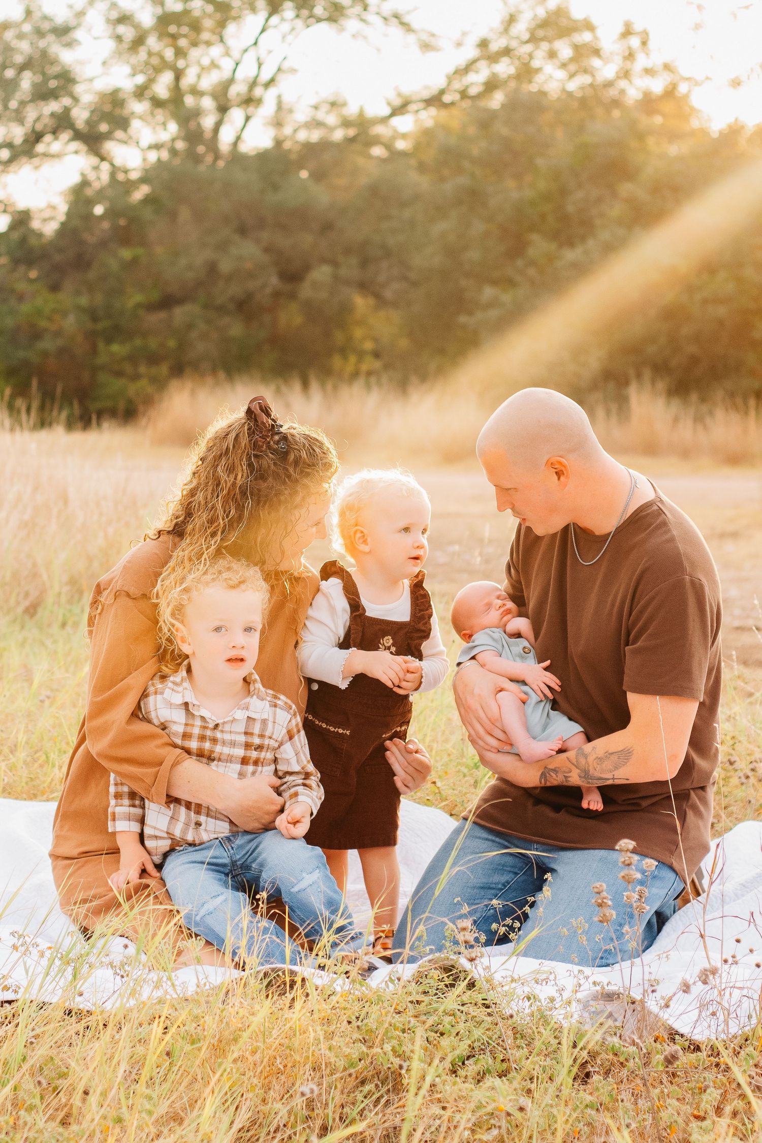 Family enjoying playful moments together on blanket in sunlit field during golden hour.