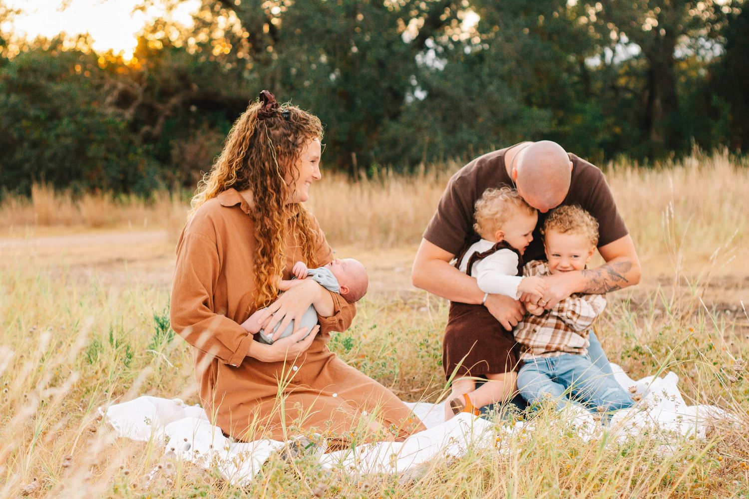 Family spending time together on a blanket in a sunlit meadow.