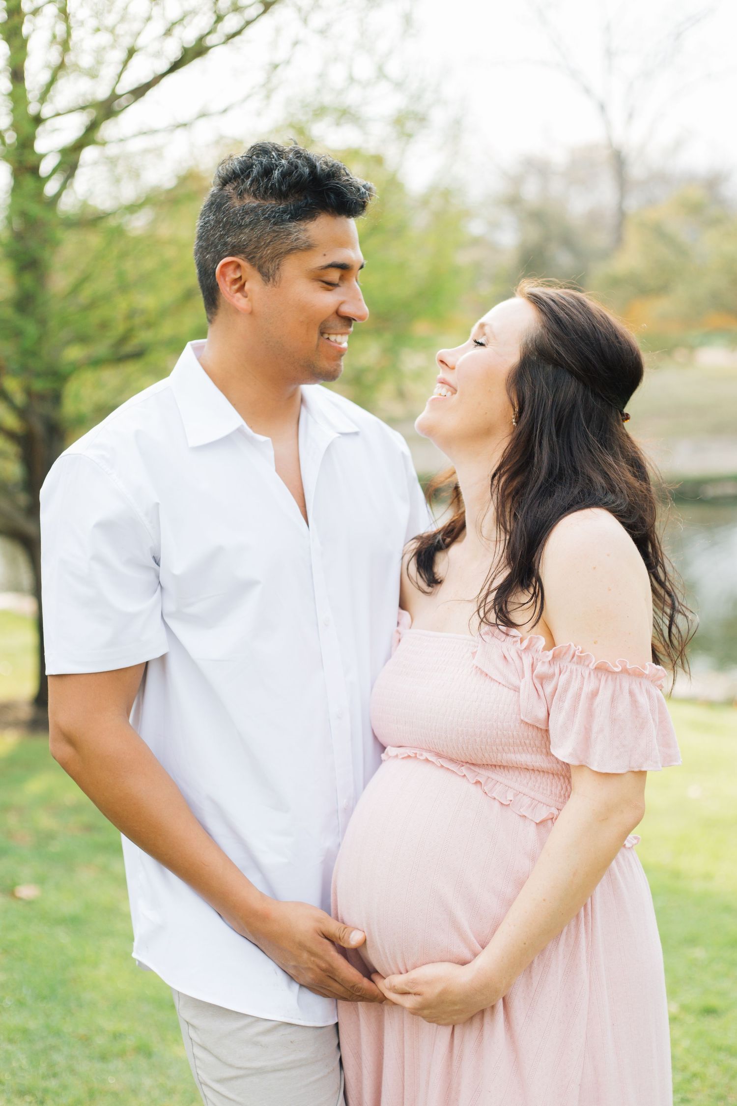 Intimate maternity photoshoot of couple in coordinated outfits against a natural outdoor backdrop.