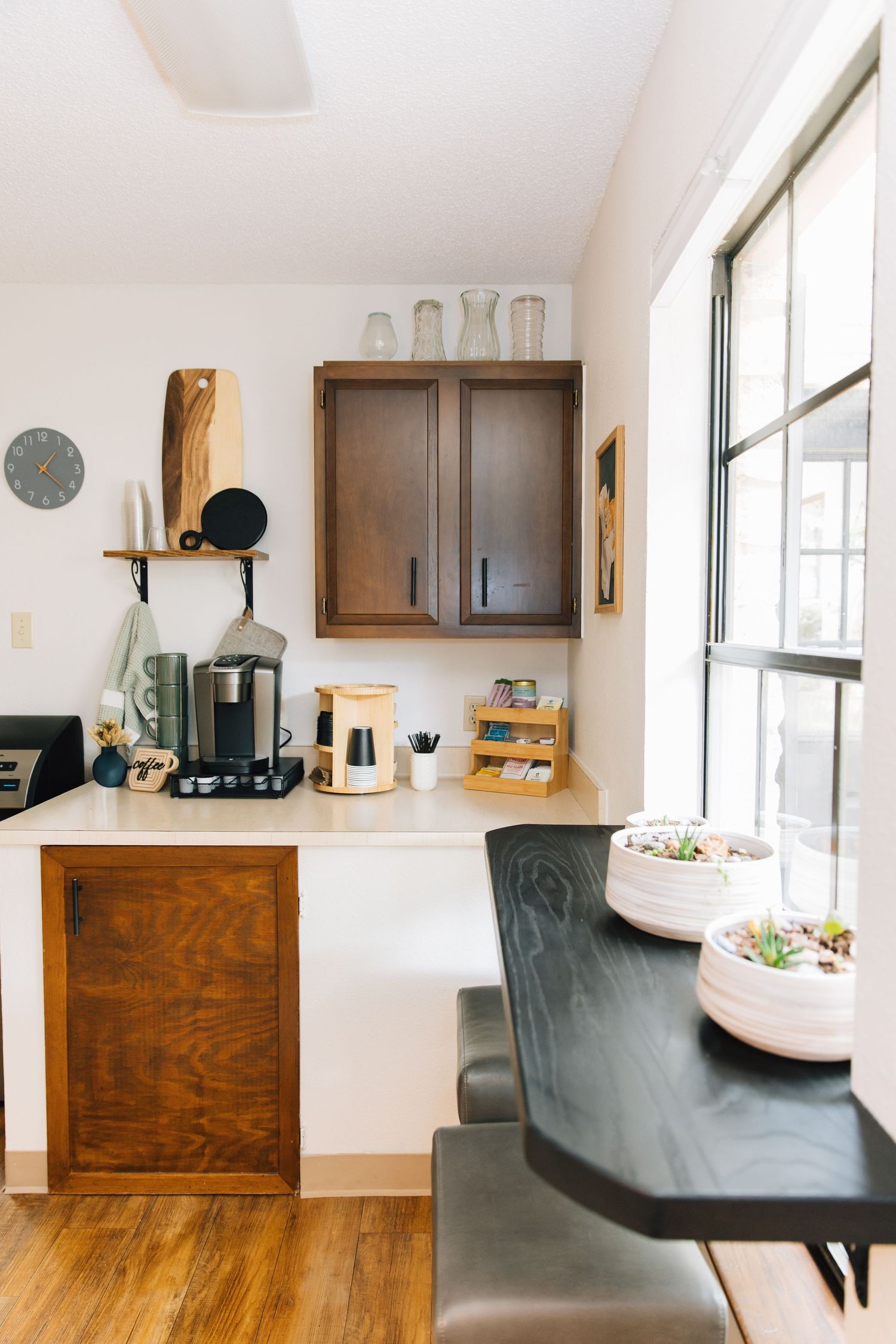 Cozy kitchen nook with dark wood cabinets, coffee station, hardwood floors, and a dining table near a large window.