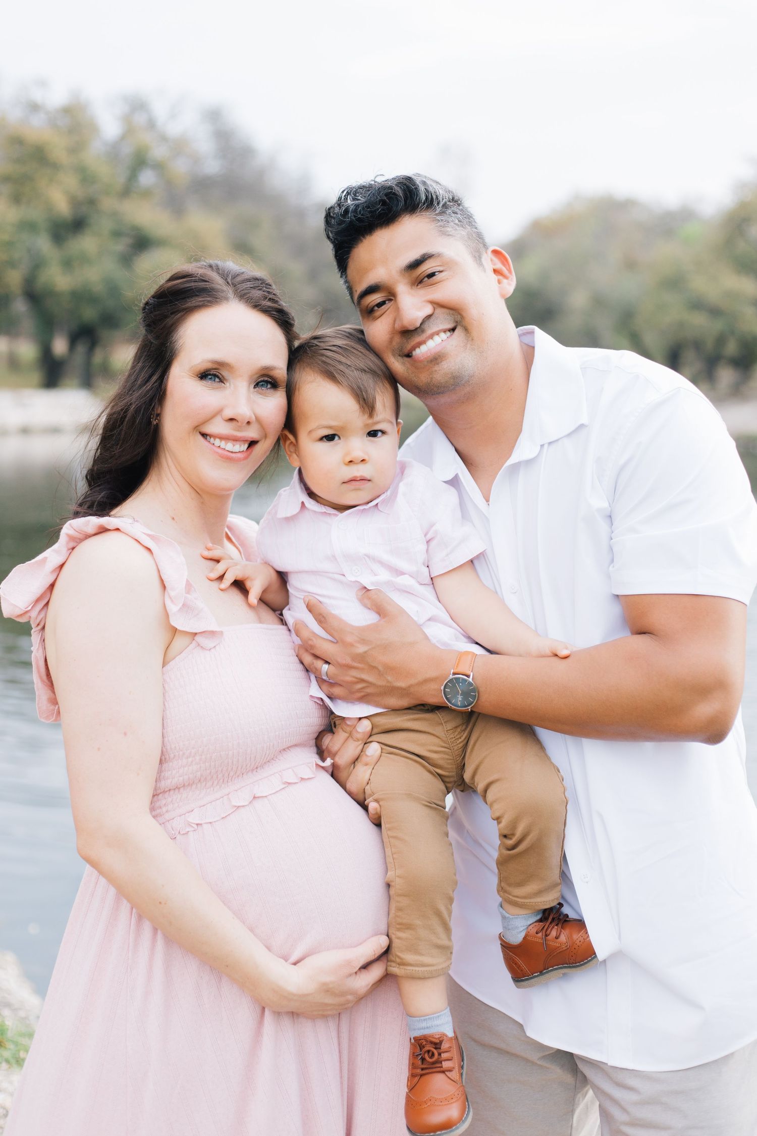 A family shares tender moments together during an outdoor photoshoot by a lake in soft lighting.