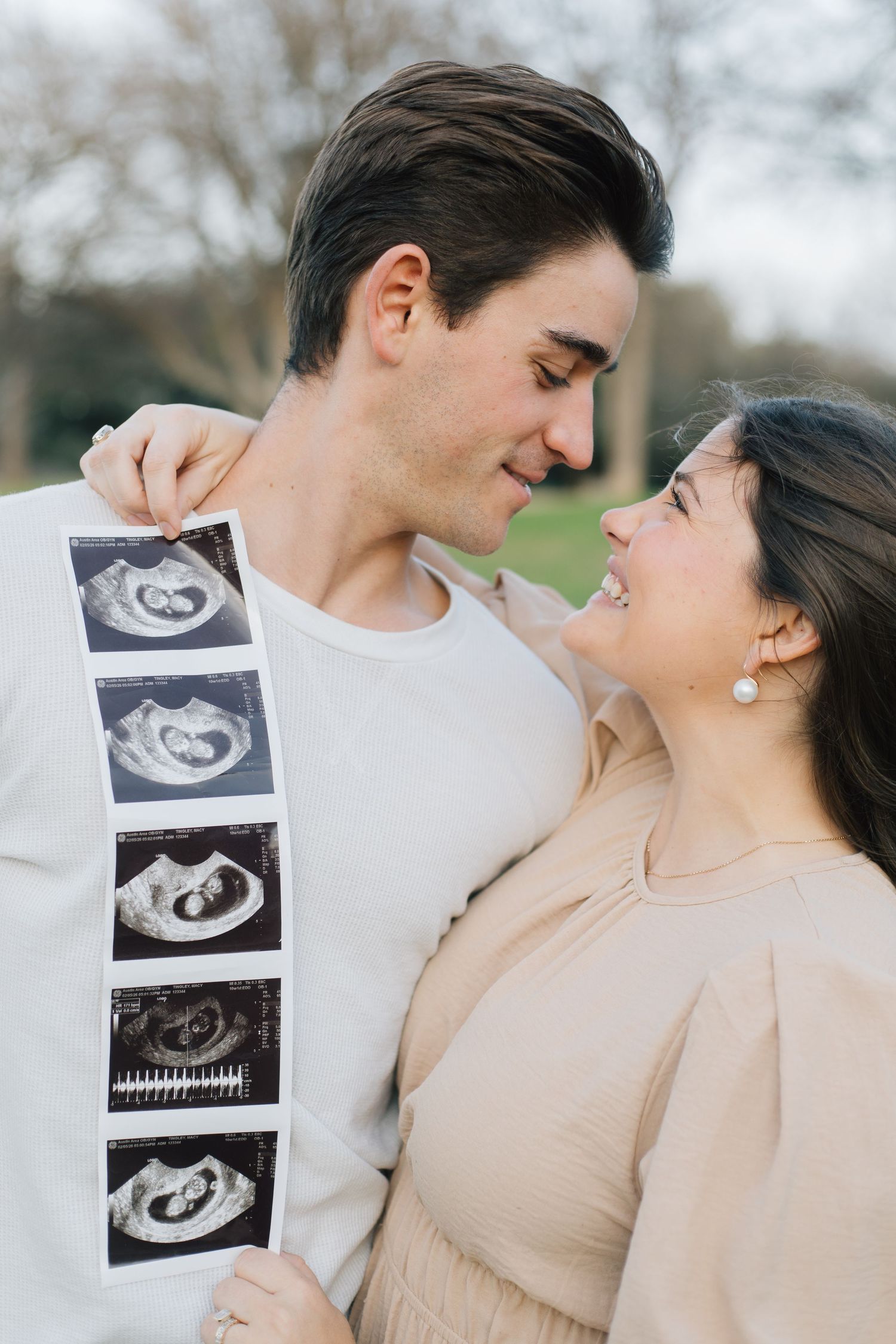 Couple shares joyful moment outdoors while displaying strip of ultrasound photos.