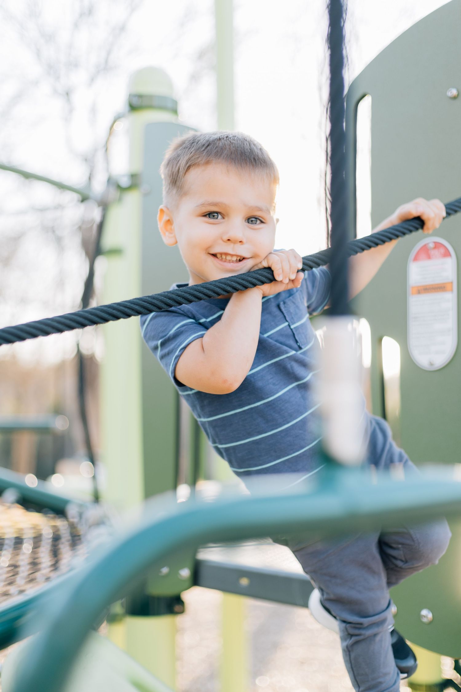 Young child playing on playground equipment in striped shirt.