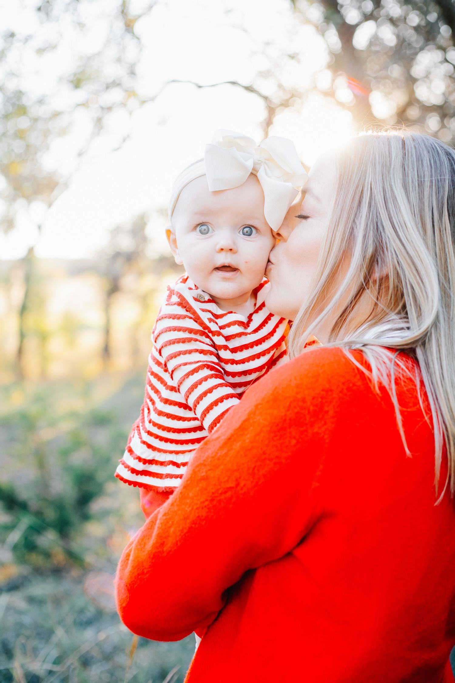 Parent in bright red sweater holds baby in striped outfit during golden hour photoshoot.