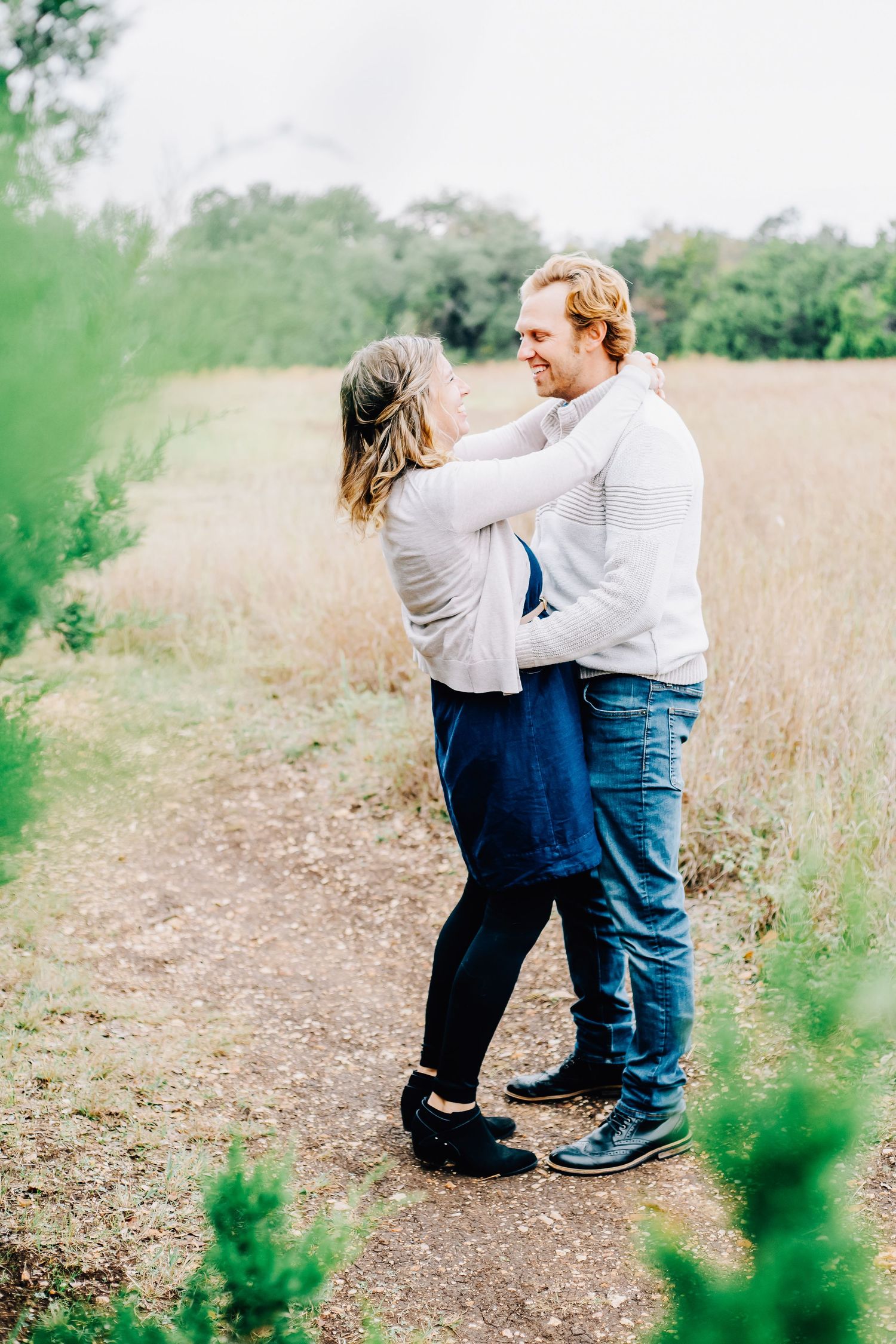 A couple embraces on a nature trail surrounded by green foliage.