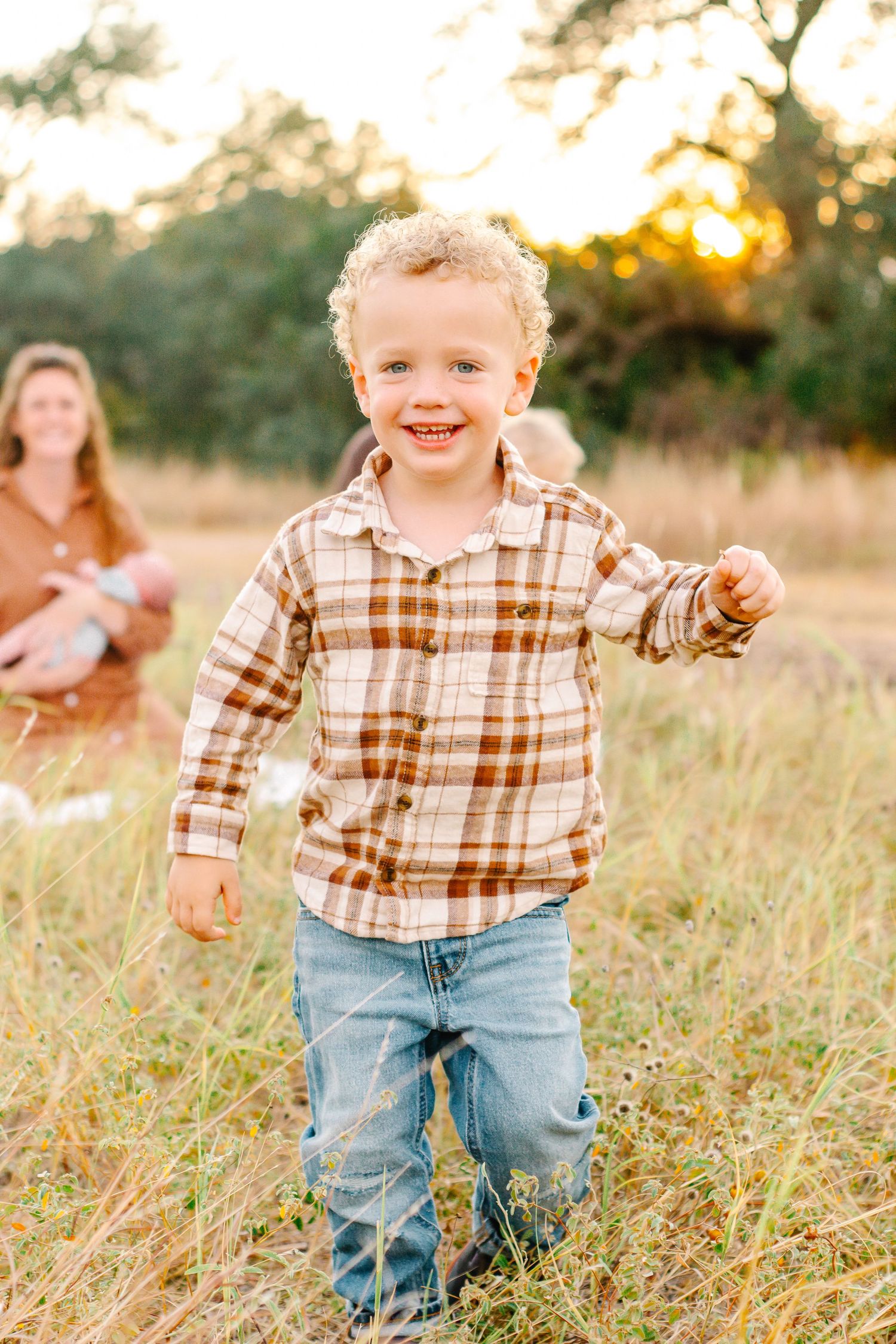 Child in plaid shirt and jeans running through tall grass at sunset.