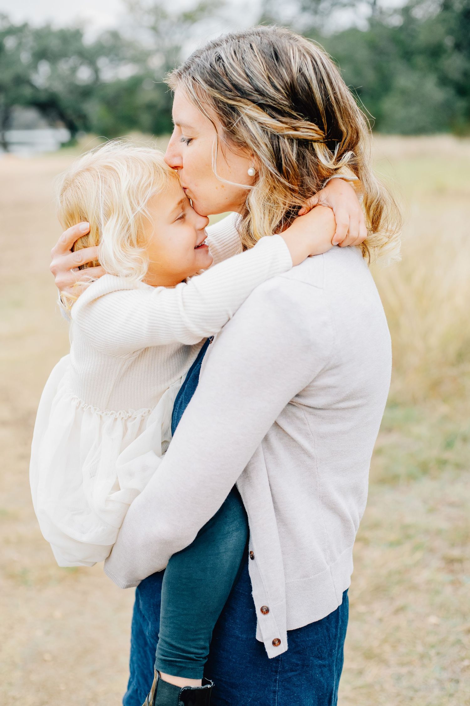 Two people in white and navy outfits embrace tenderly in a sunlit outdoor field.