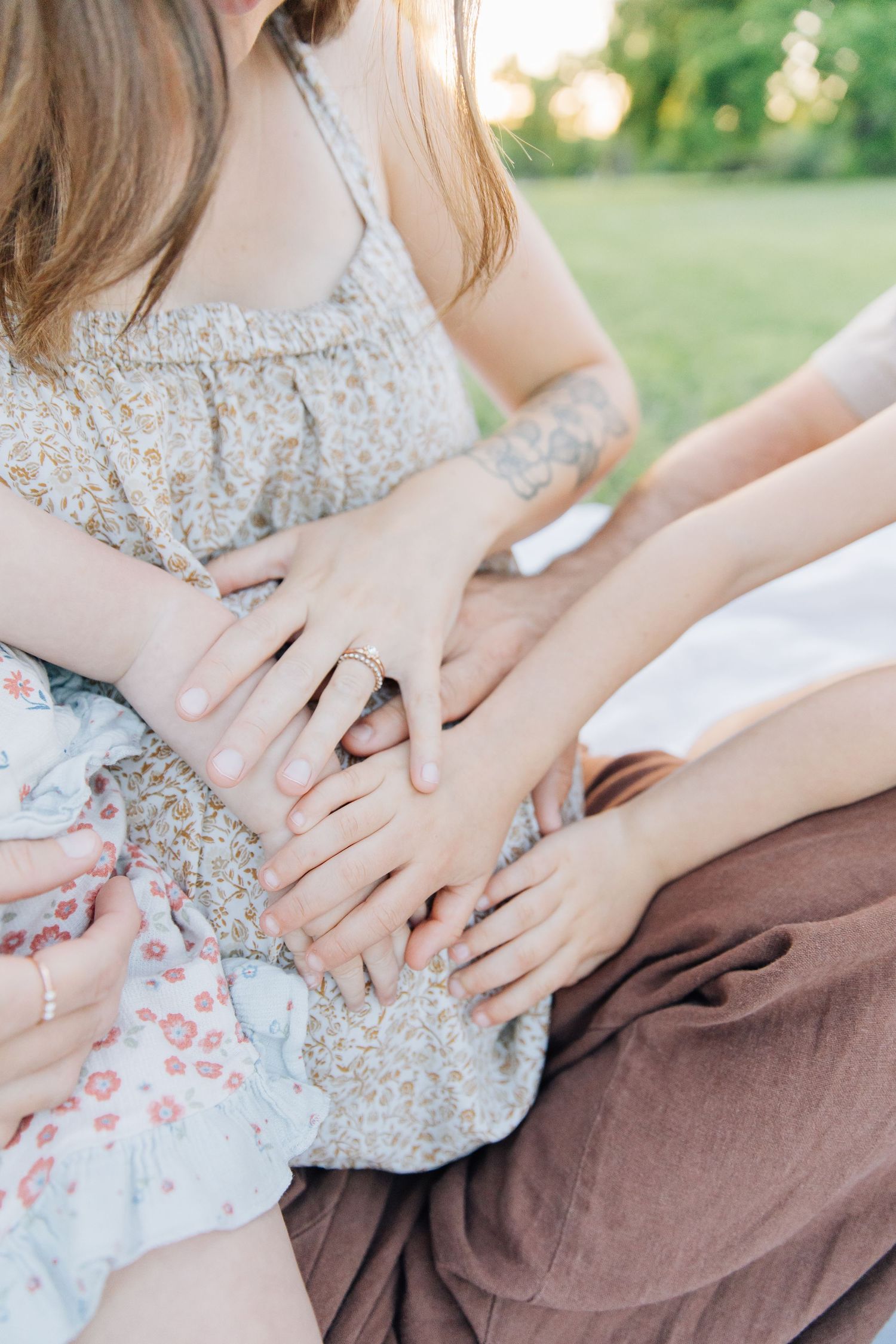 Close-up of a family holding hands together on laps during an outdoor gathering in nature.