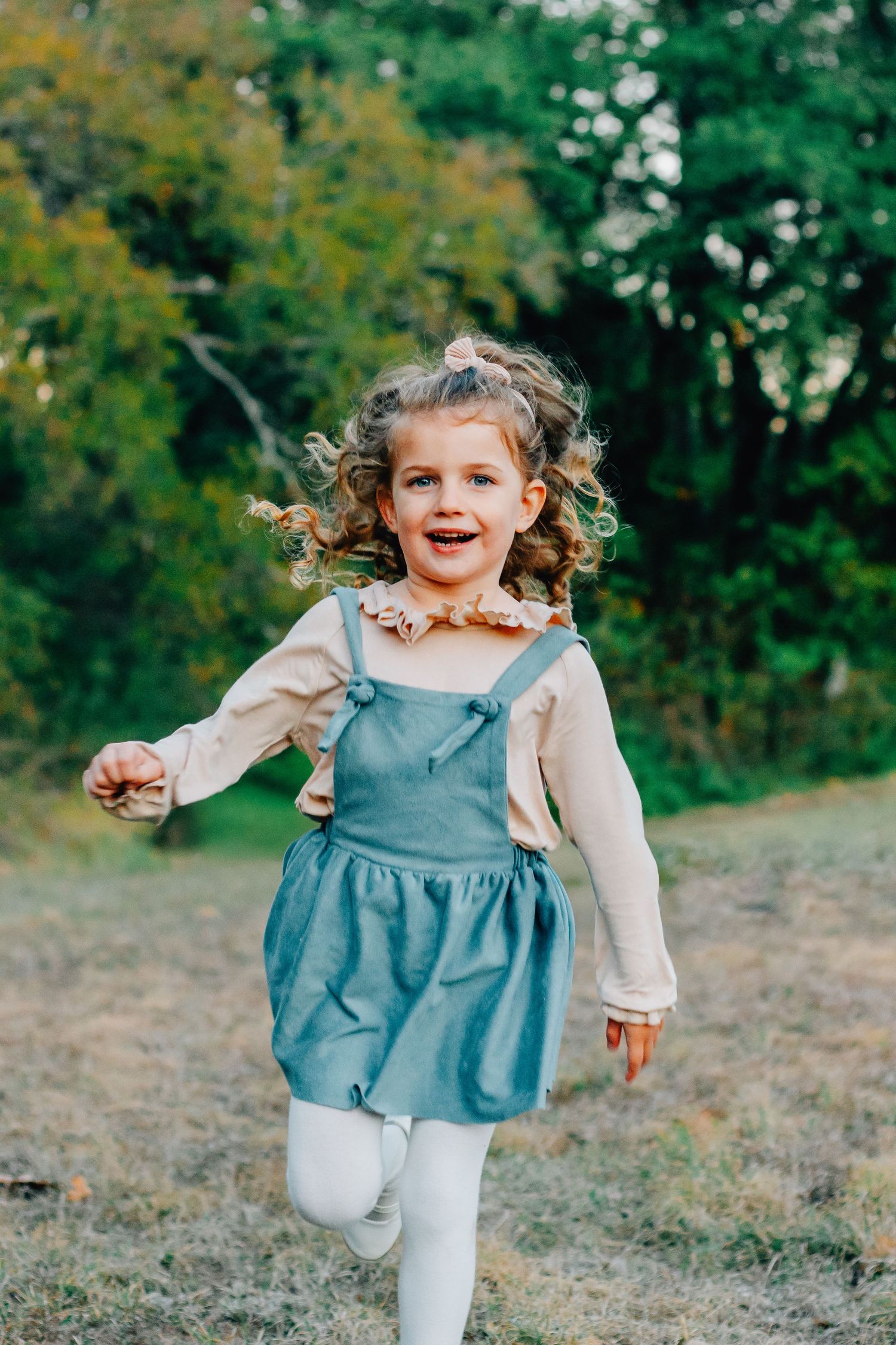 Energetic toddler in blue dress and white tights running and playing outdoors.