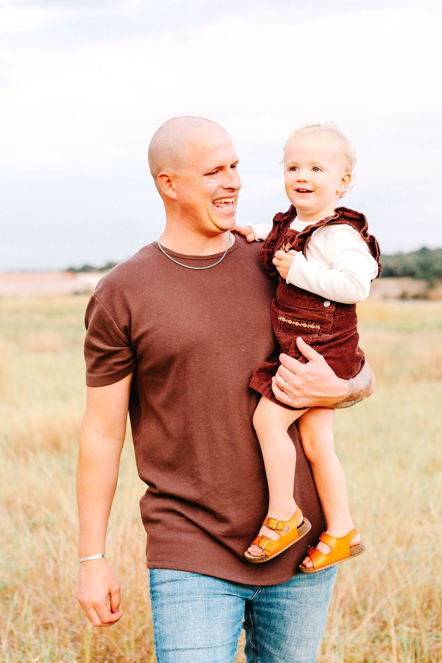 Person in brown shirt holding child in casual outdoor setting during sunset.
