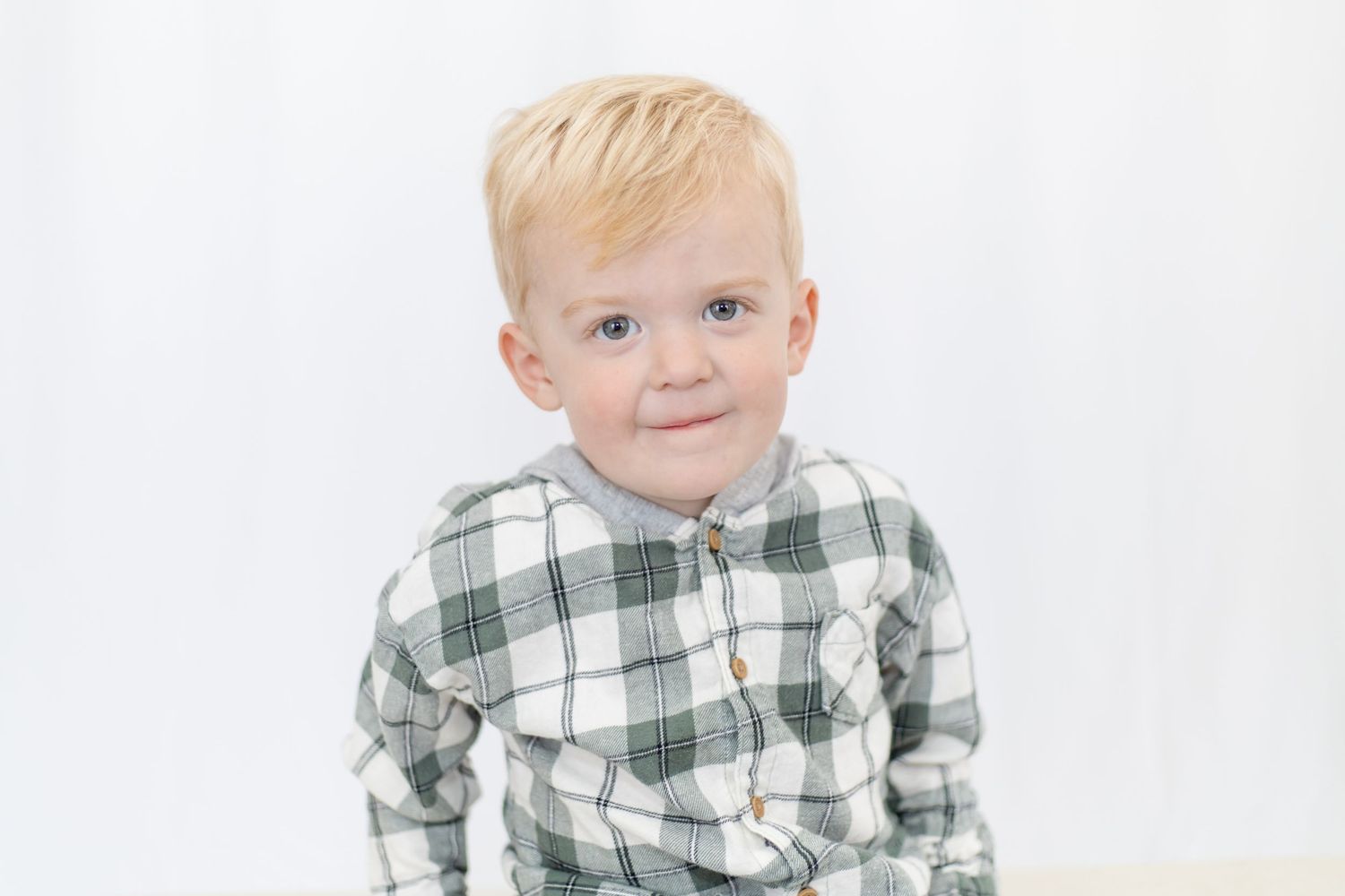 Child in green and white plaid shirt posing against white background.
