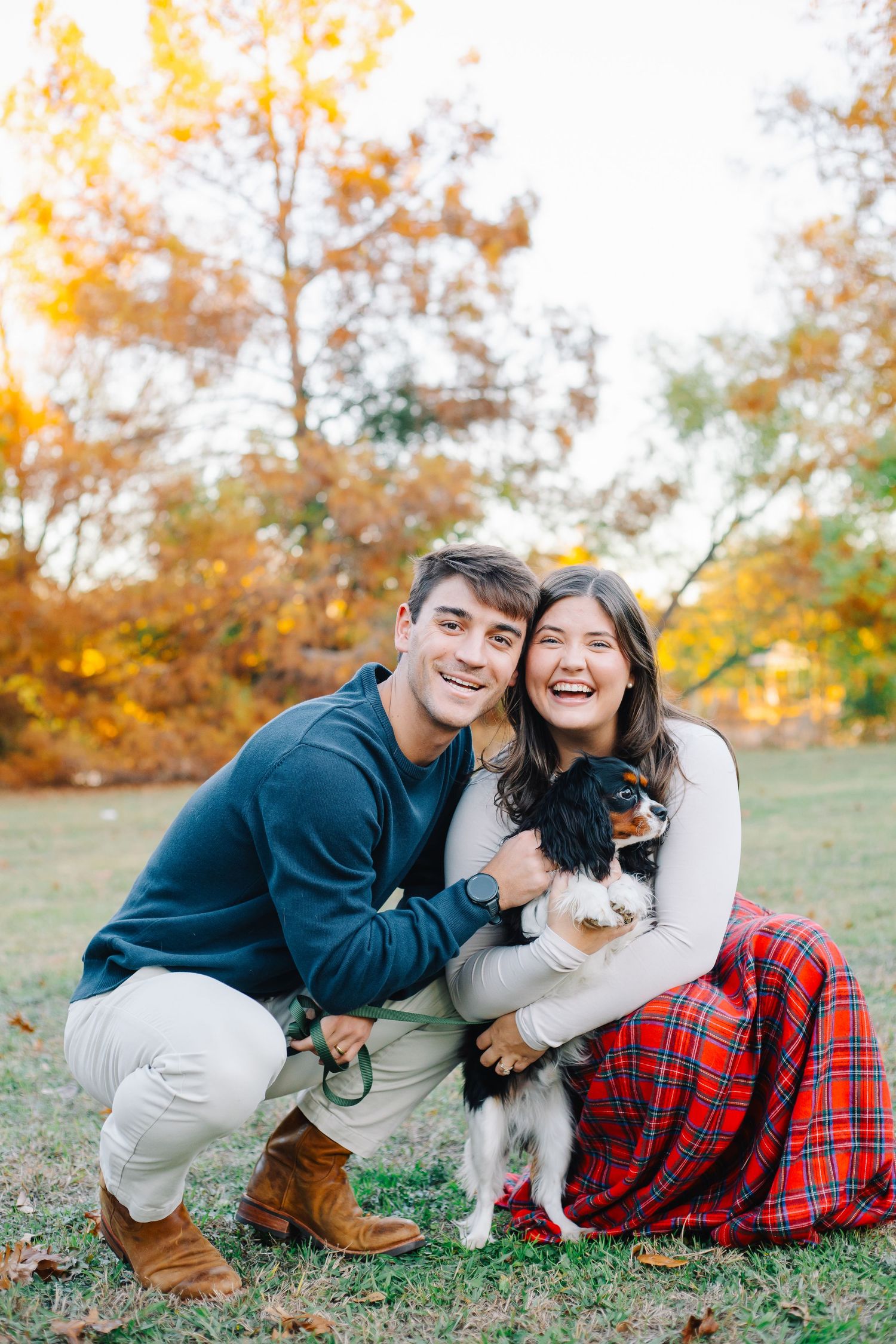 Couple poses playfully with their dog on grass during fall photo session.