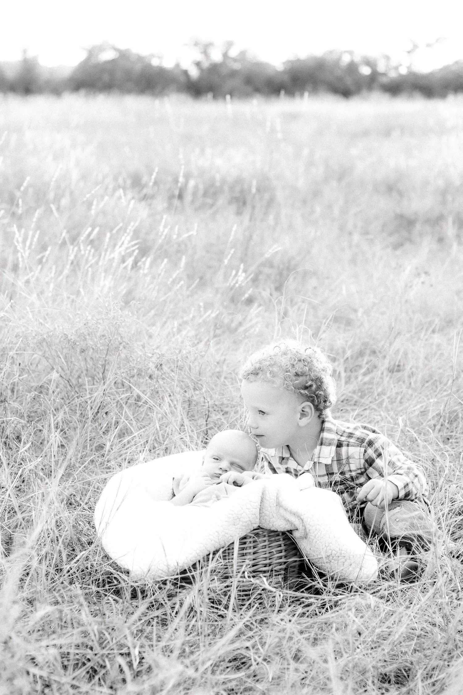 Black and white photo of family lying together in tall grass field.