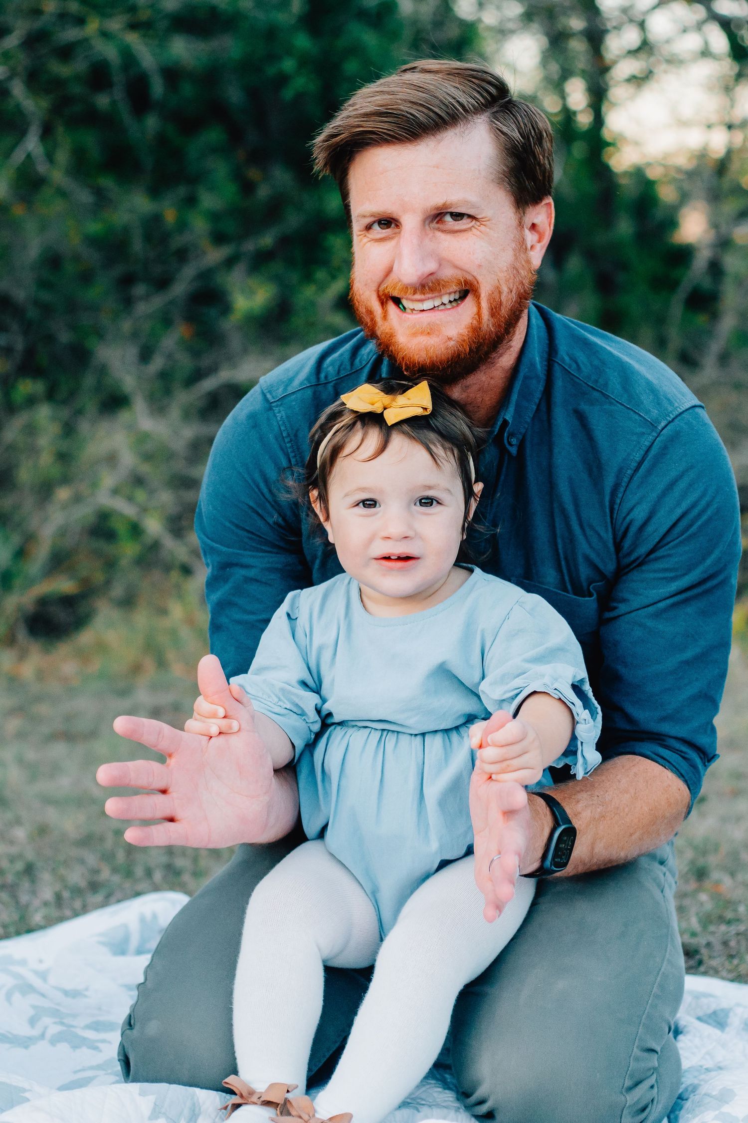 Sweet interaction between parent and child in blue dress sitting on ground during outdoor photoshoot.