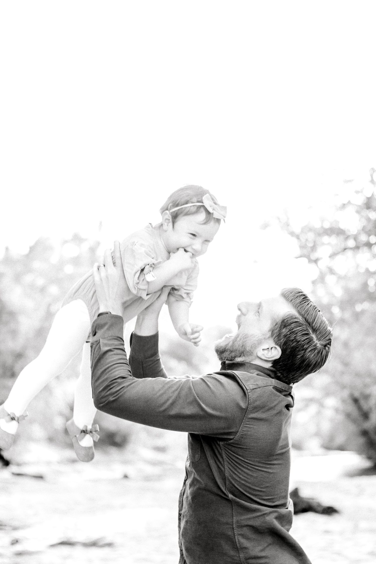 Black and white series of parent lifting and playing with child outdoors.