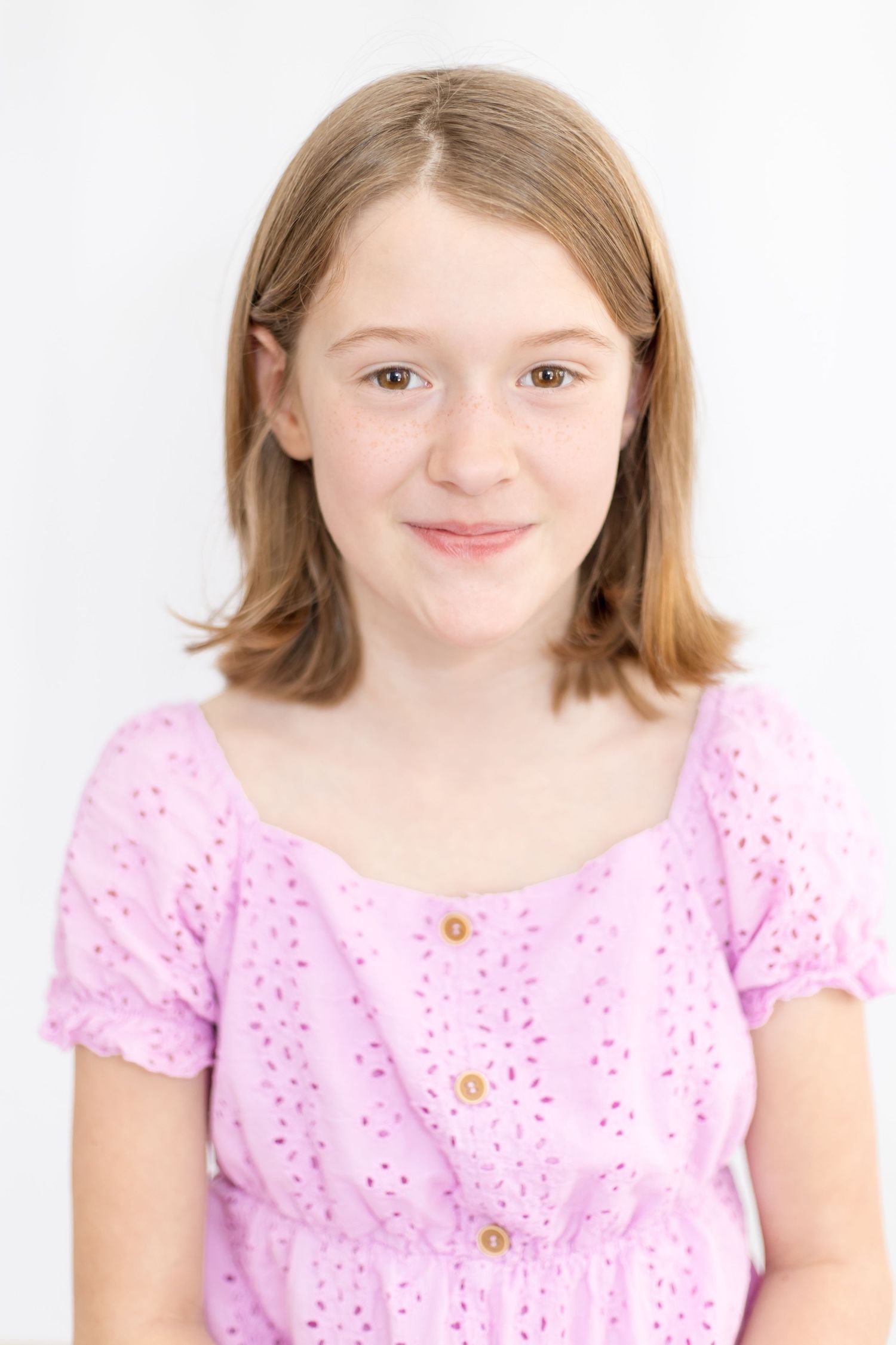Girl wearing pink eyelet dress with short sleeves smiling at camera.