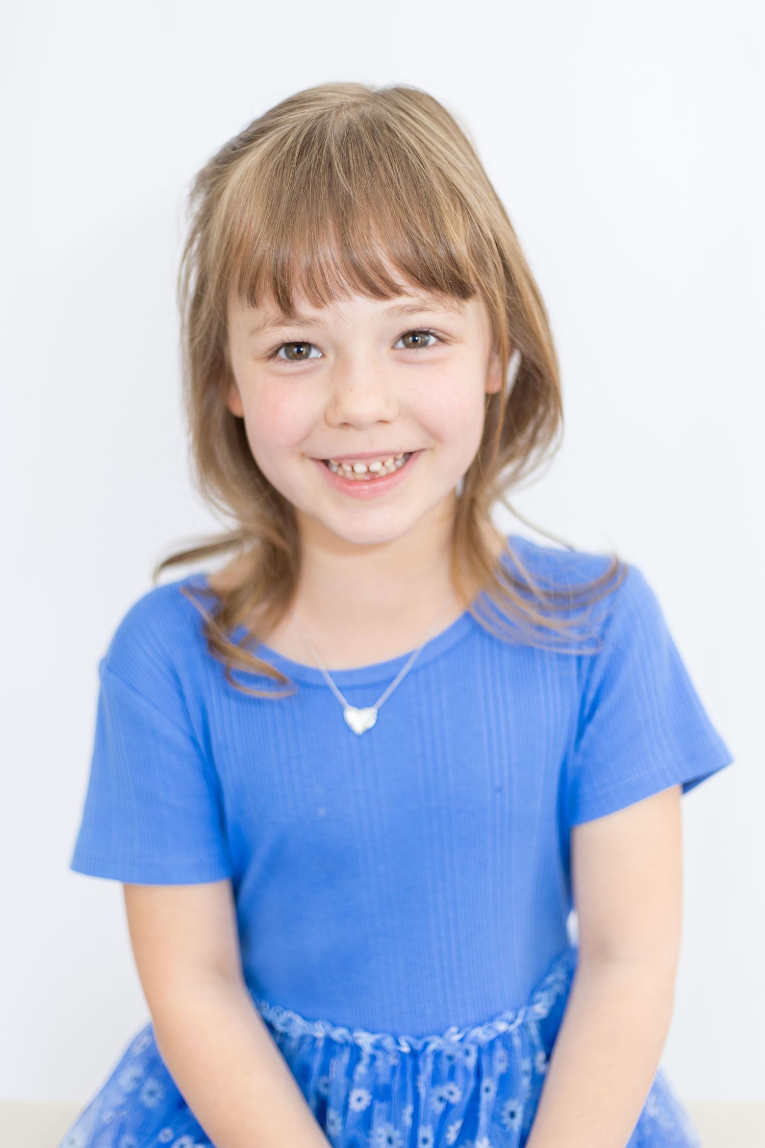 Child wearing blue dress smiles during studio portrait session.