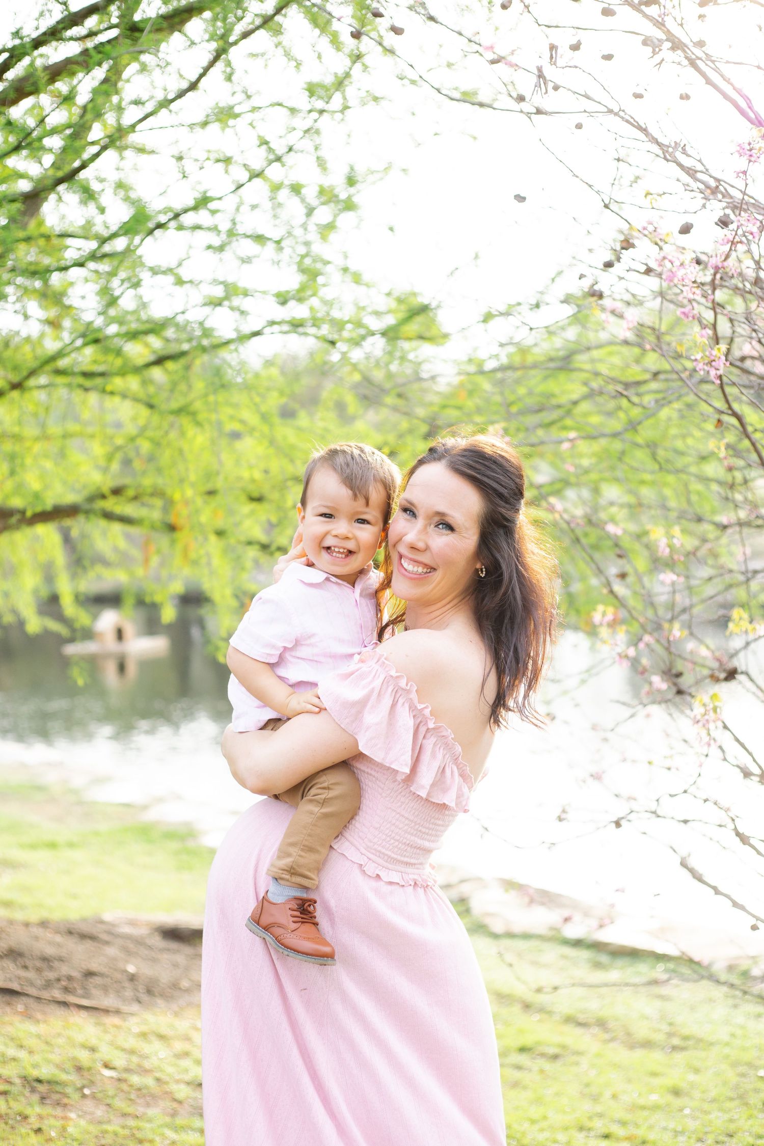 A woman in a pink dress shares joyful moments with a toddler during a spring photoshoot.