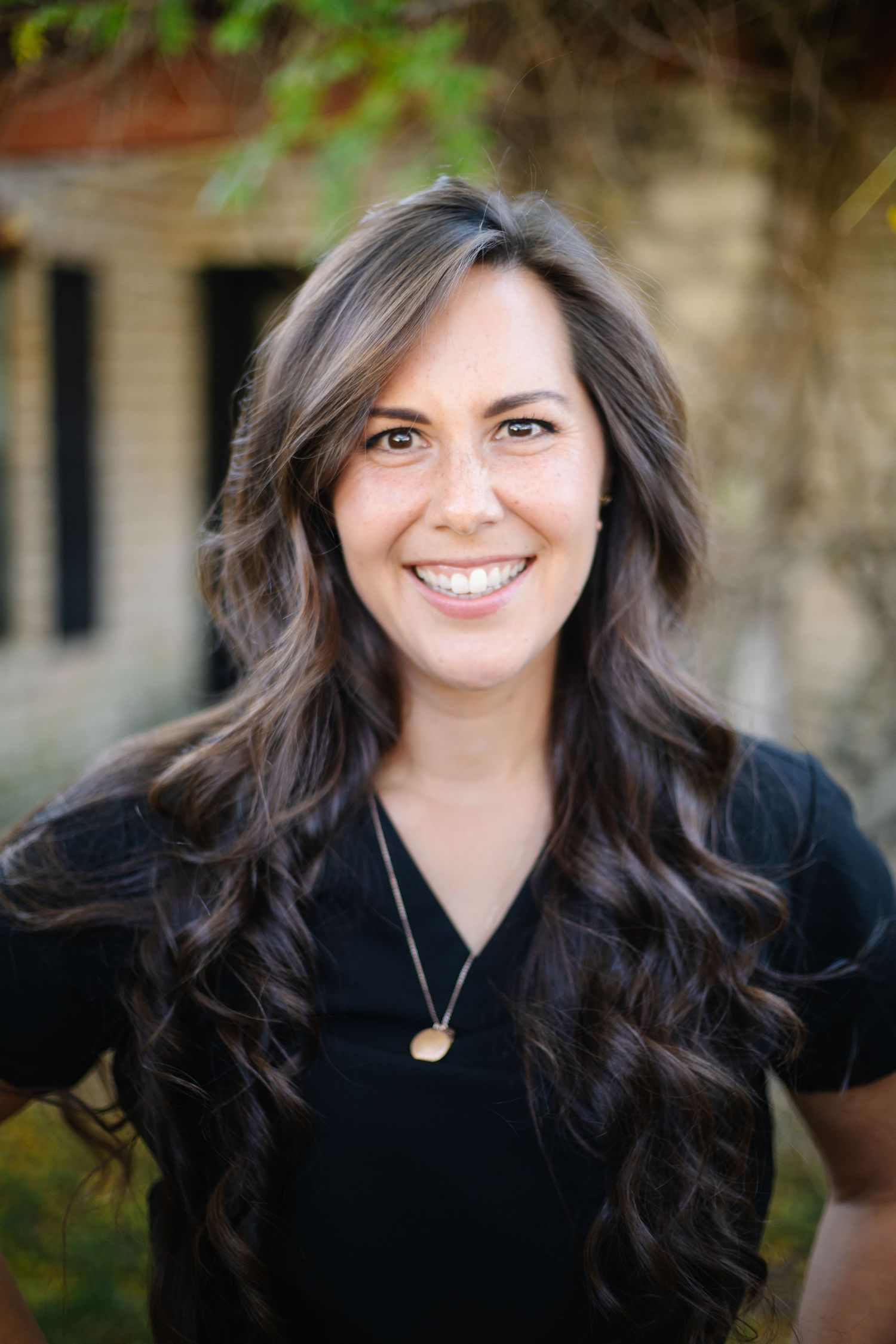 A professional headshot of a veterinary staff member wearing black against a blurred outdoor background.