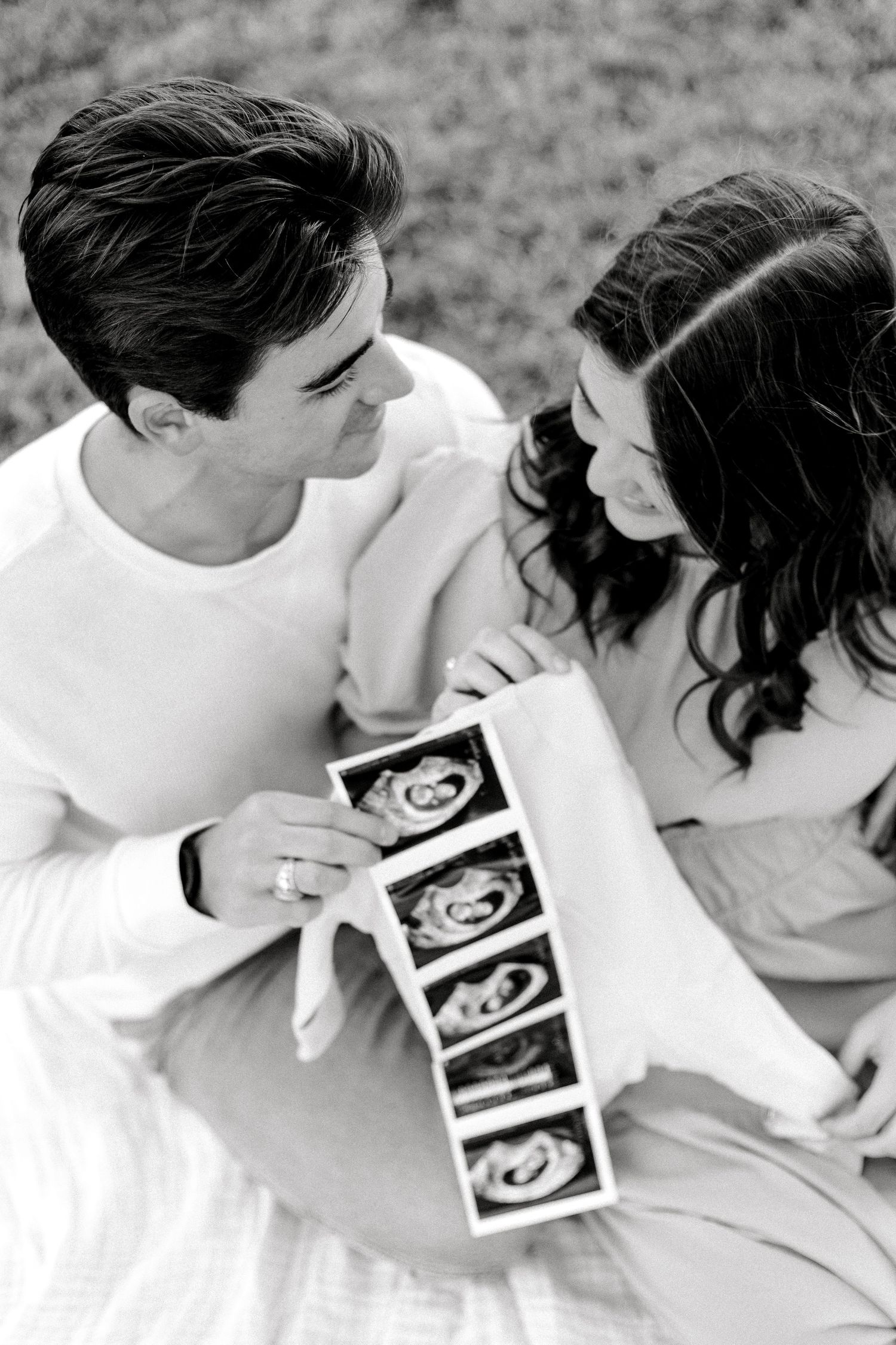 Black and white photo of couple sharing intimate moment while holding ultrasound strip.