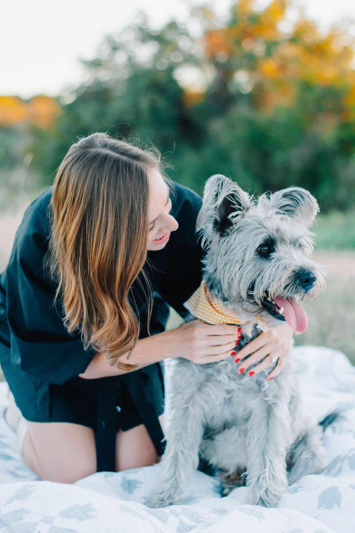 A person in black cuddles with a gray terrier on a white blanket outdoors.