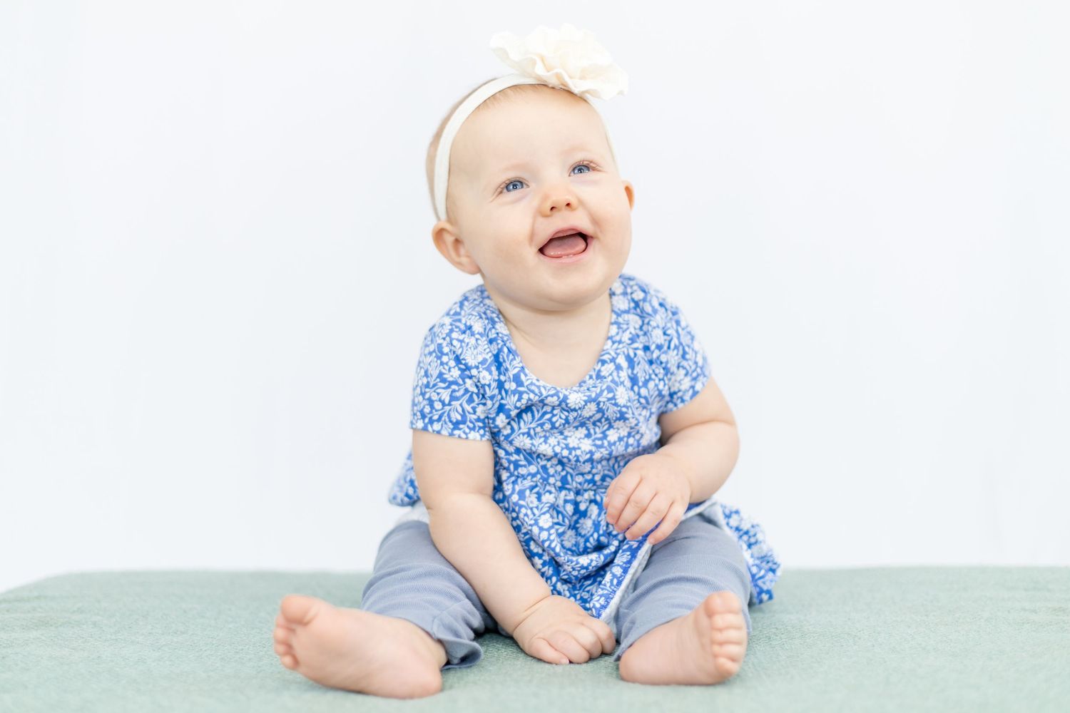 Smiling baby wearing blue floral dress and white bow headband.