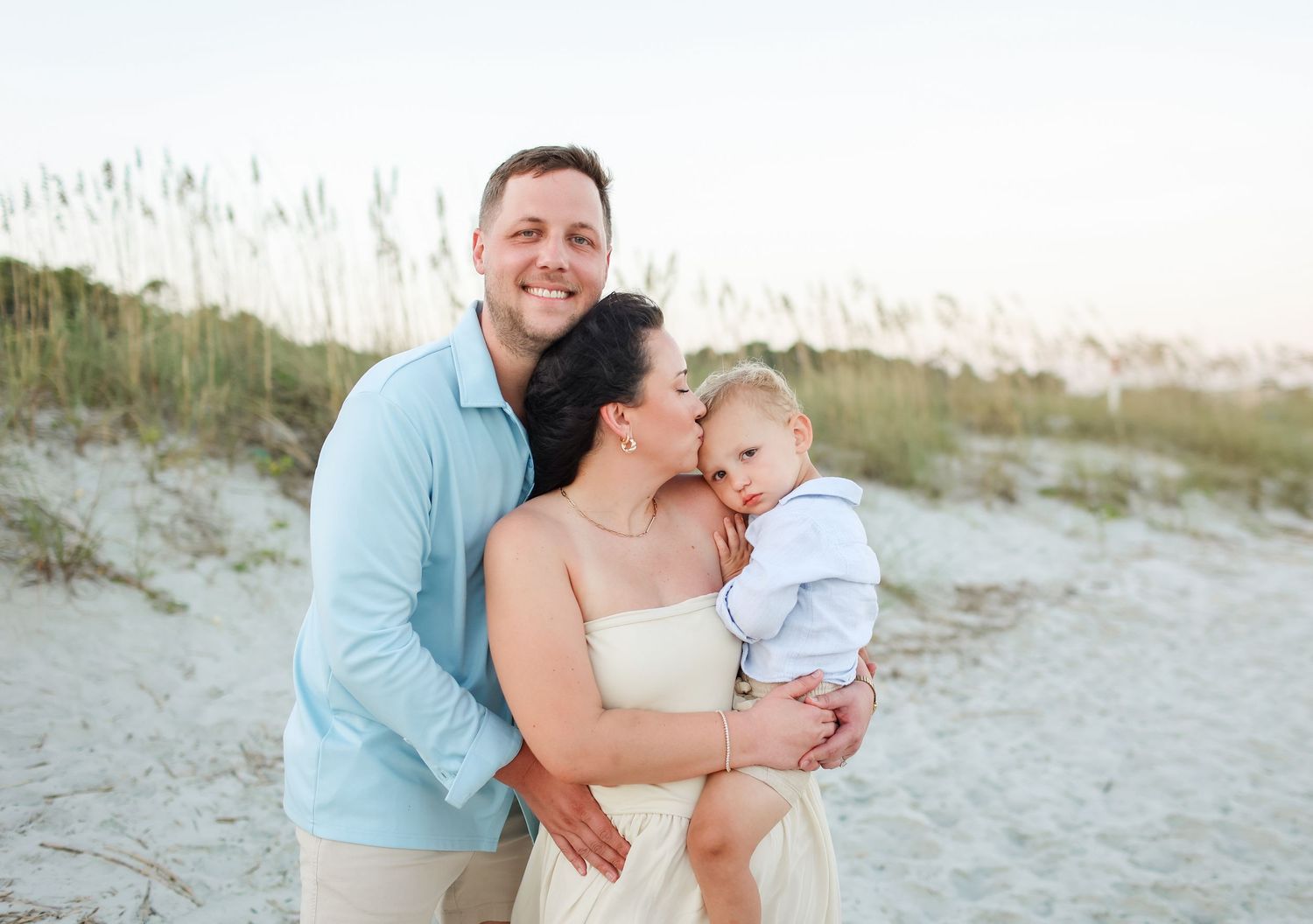 Hilton Head family photography capturing parents kissing their baby in a close embrace at Folly Field Beach