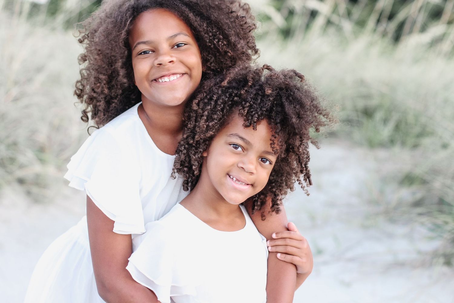 Hilton Head family photography of two sisters hugging in the sand dunes at sunrise on Folly Field Beach