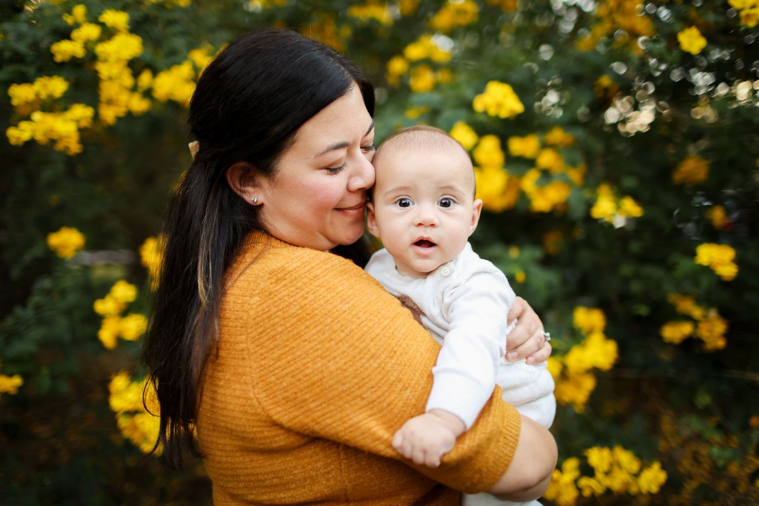 Hilton Head family photography of a mother holding her newborn beside bright yellow winter cassia flowers