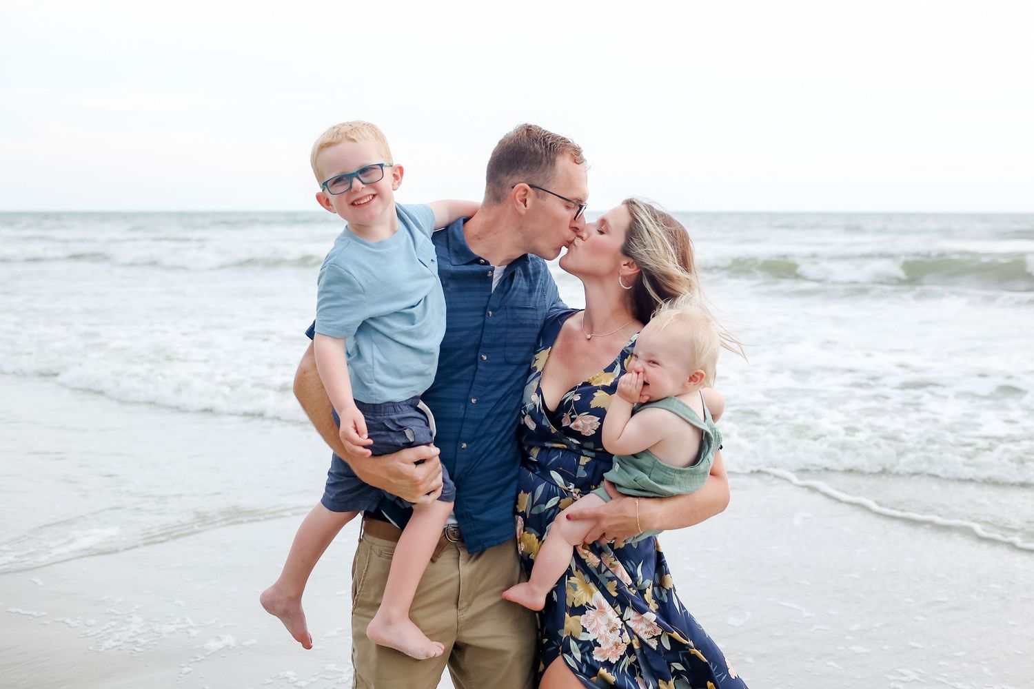 Hilton Head family photography of parents kissing while holding their children at sunset in Sea Pines Beach Club