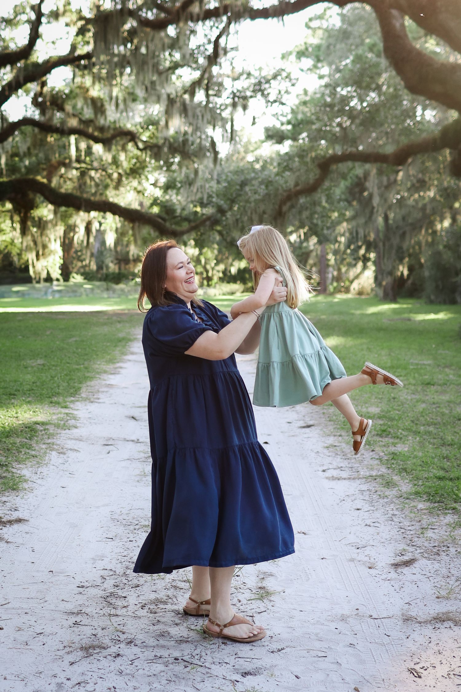 Hilton Head family photography capturing a mother tossing her toddler under live oak trees and Spanish moss at sunset