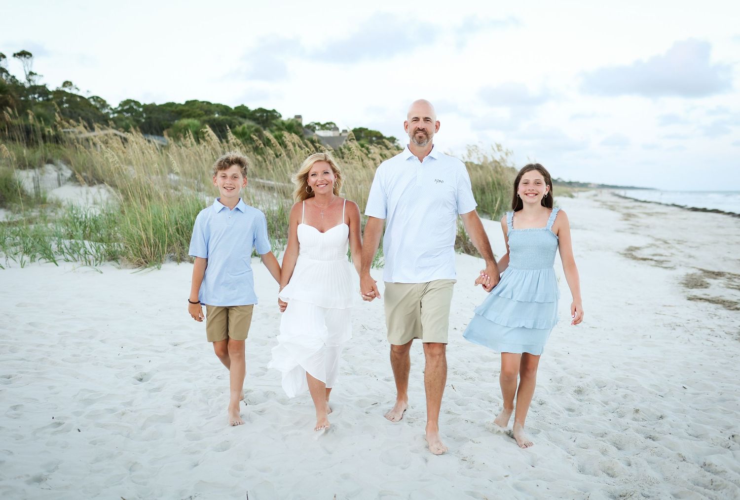 Sunset family photography on Hilton Head as a family walks hand in hand through sand dunes smiling together